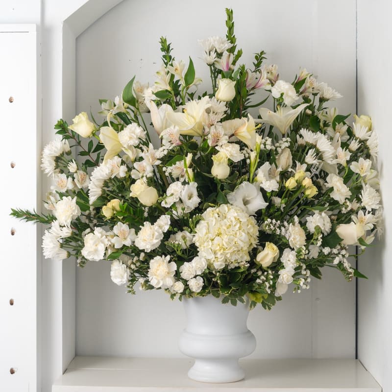Large white and cream mixed flower arrangement in a white pedestal vase