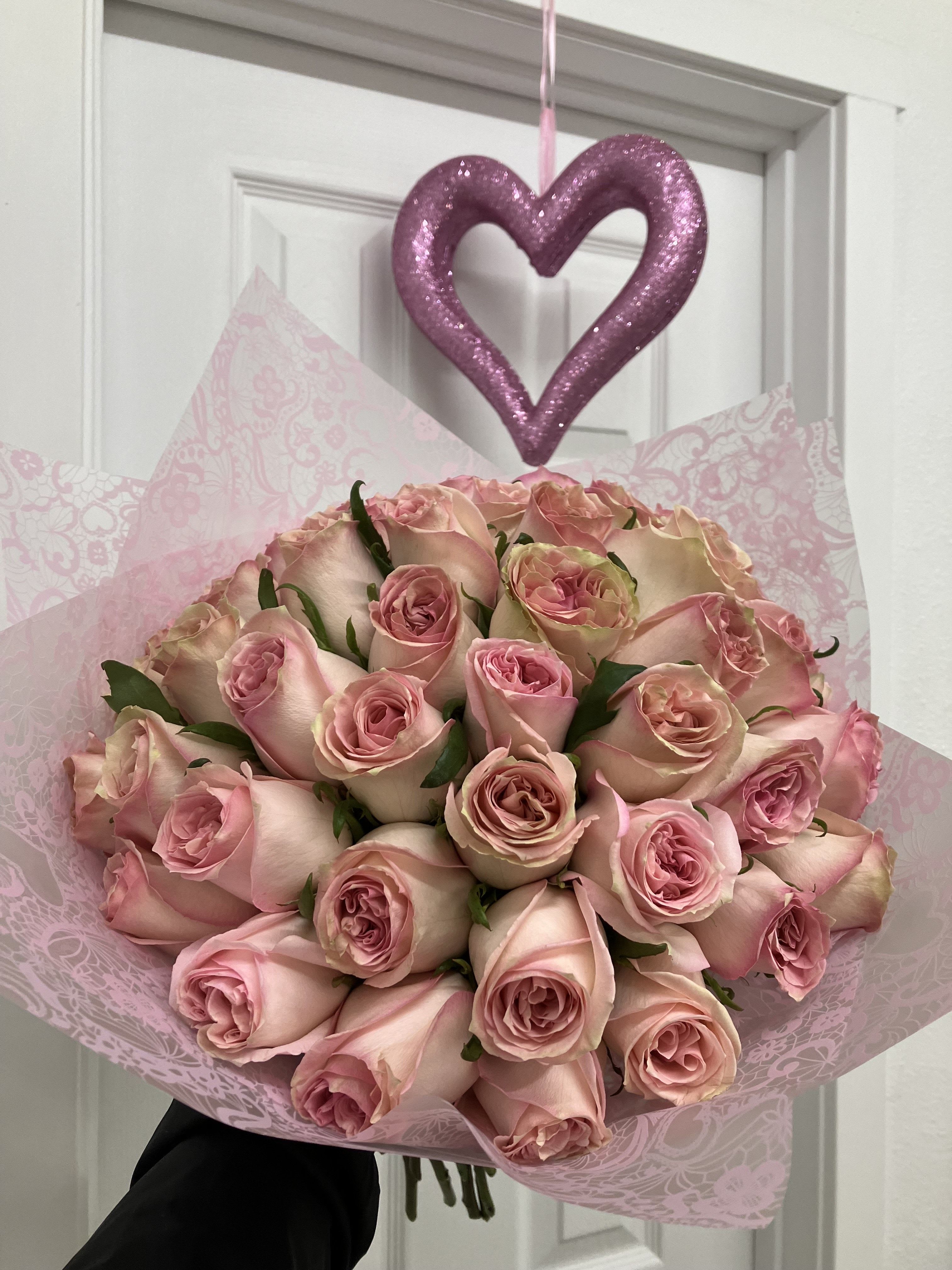 Bouquet of pale pink roses wrapped in pink paper with a glittery heart ornament