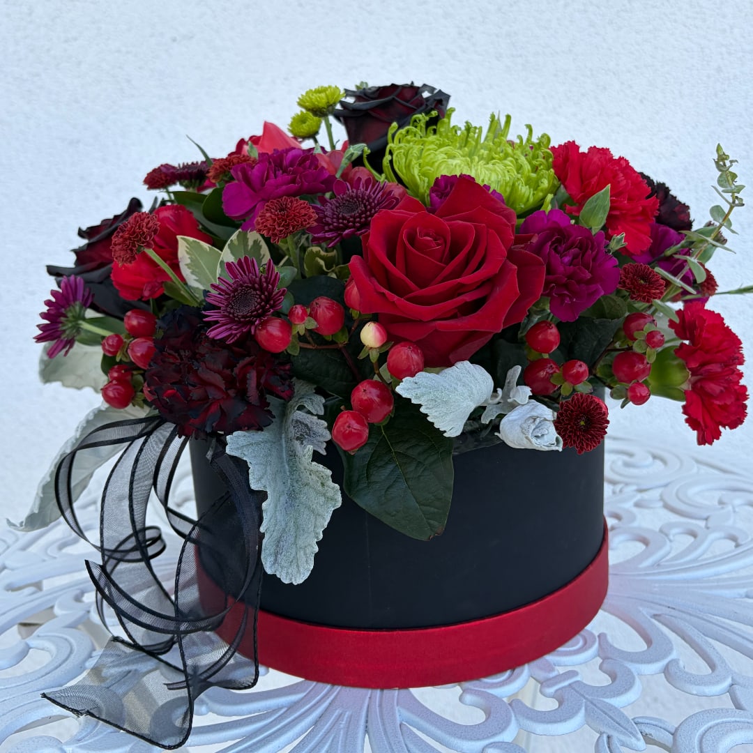 Red and purple flower arrangement in a black round box with ribbon