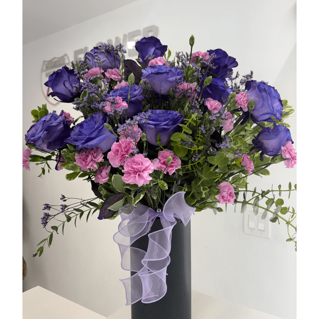 Purple roses and pink carnations in a tall black vase with a lavender ribbon