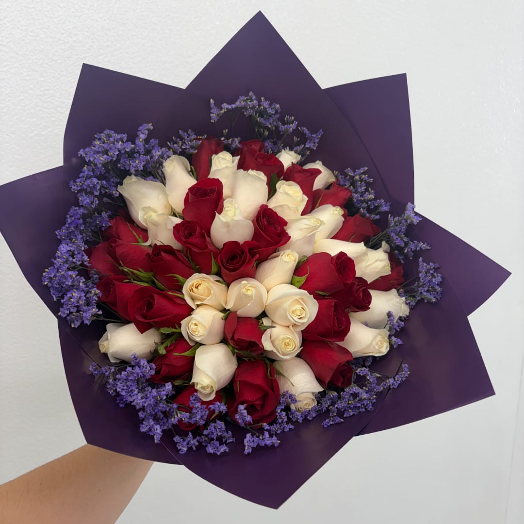 Bouquet of red and white roses with purple filler flowers in dark wrapping