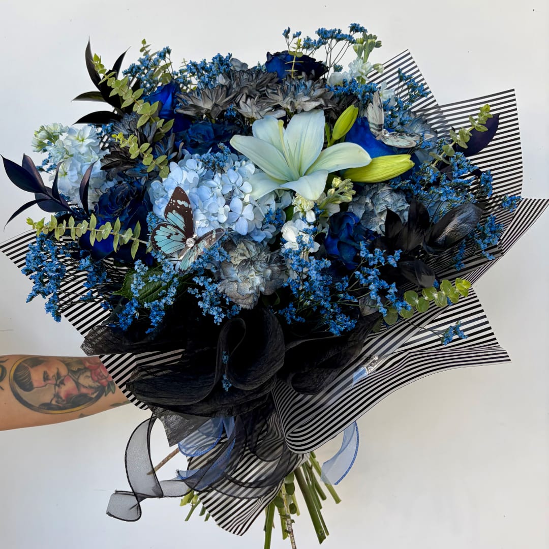 Blue and black bouquet with lilies, roses, and hydrangeas wrapped in striped paper