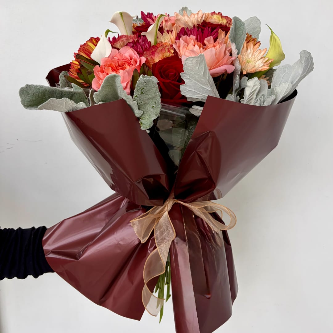 Hand-tied bouquet of mixed roses, carnations, and calla lilies wrapped in burgundy paper