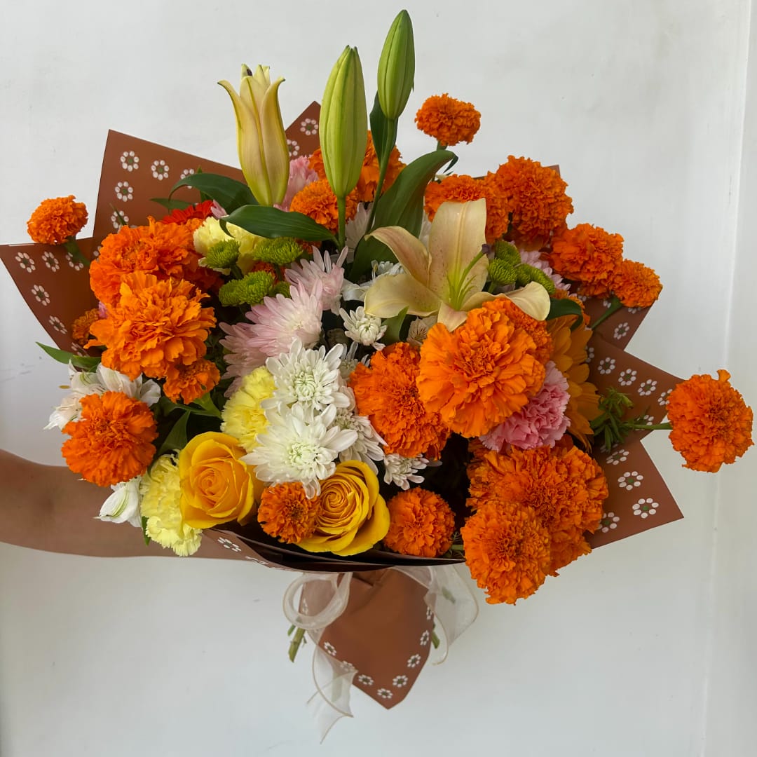 Bouquet of orange marigolds, yellow roses, and lilies wrapped in brown paper