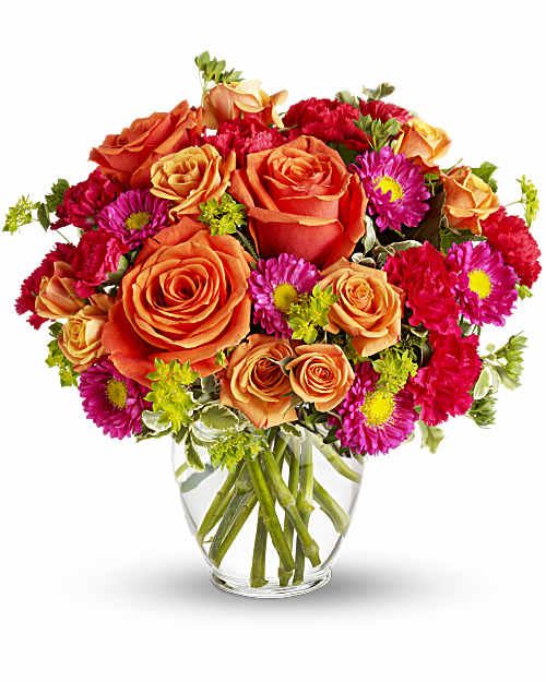 Orange roses and pink daisies in a clear glass vase