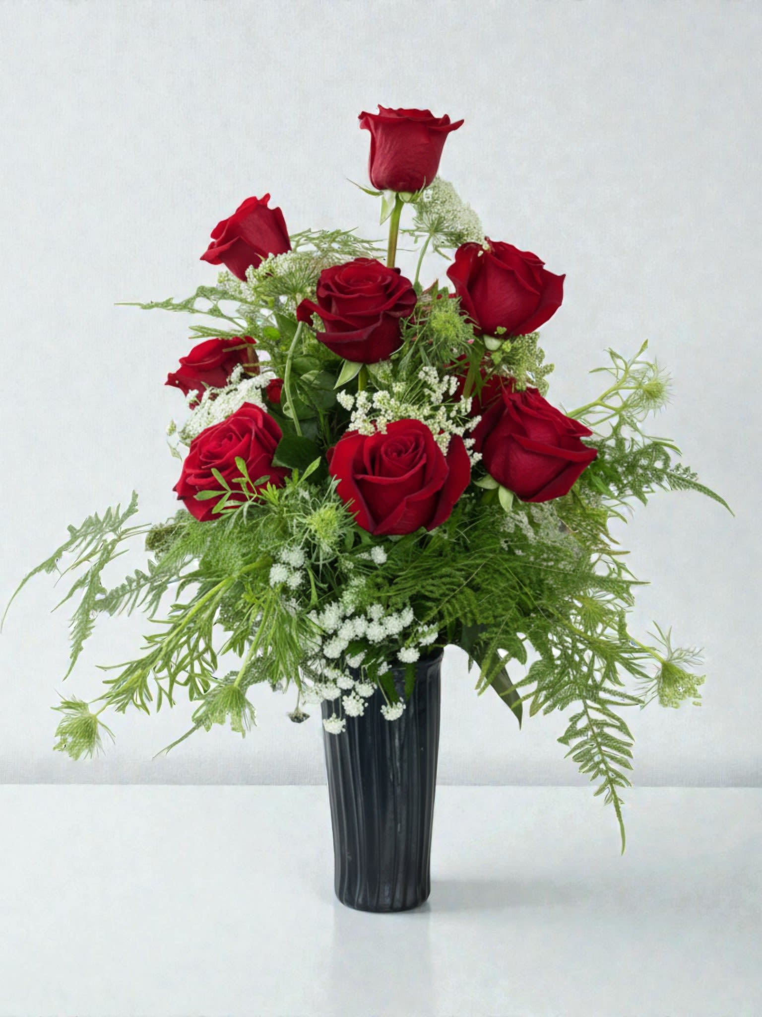 Red roses arranged in a black vase with airy white filler flowers