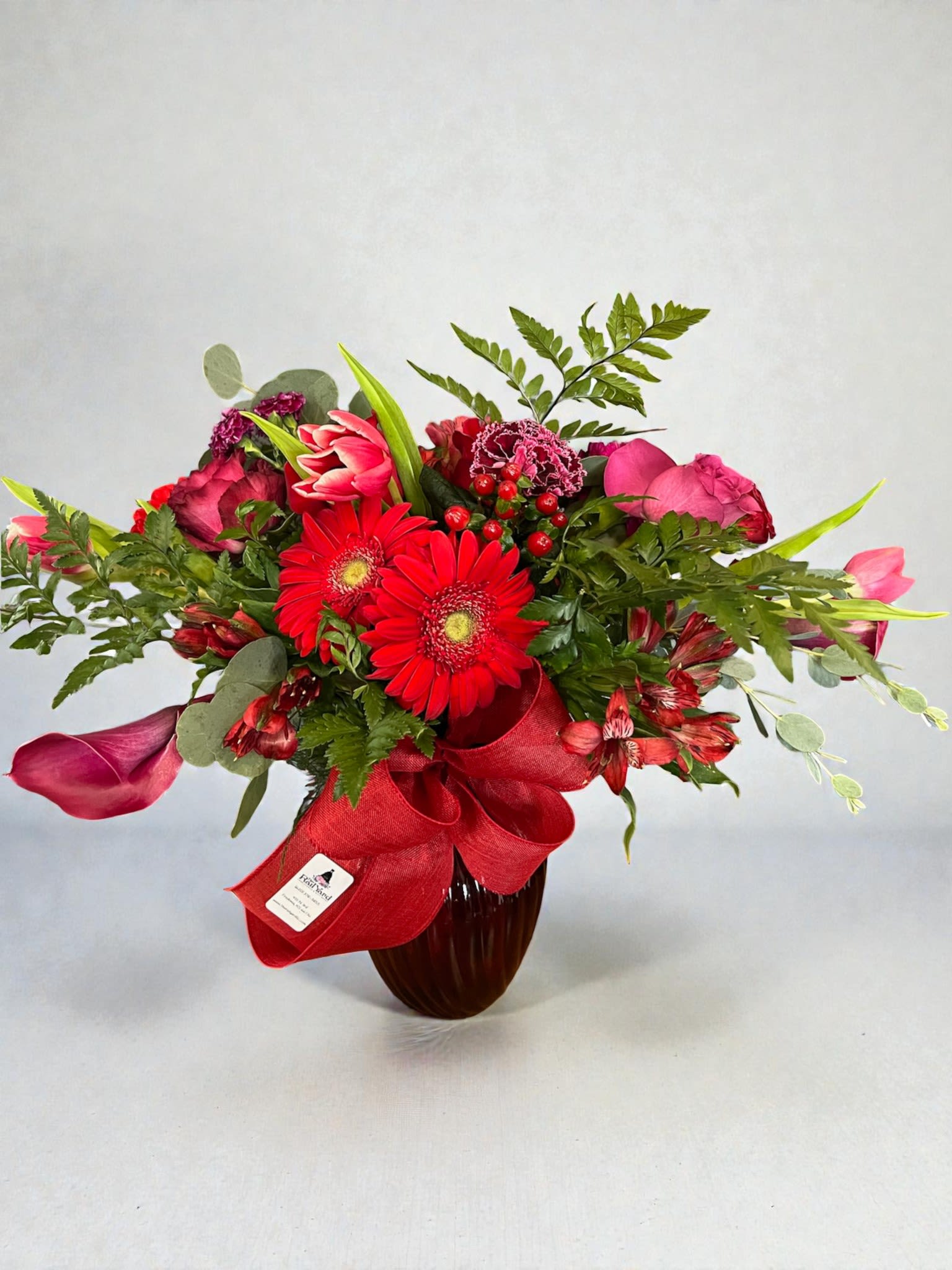 Red and pink mixed bouquet in a dark vase with a red ribbon