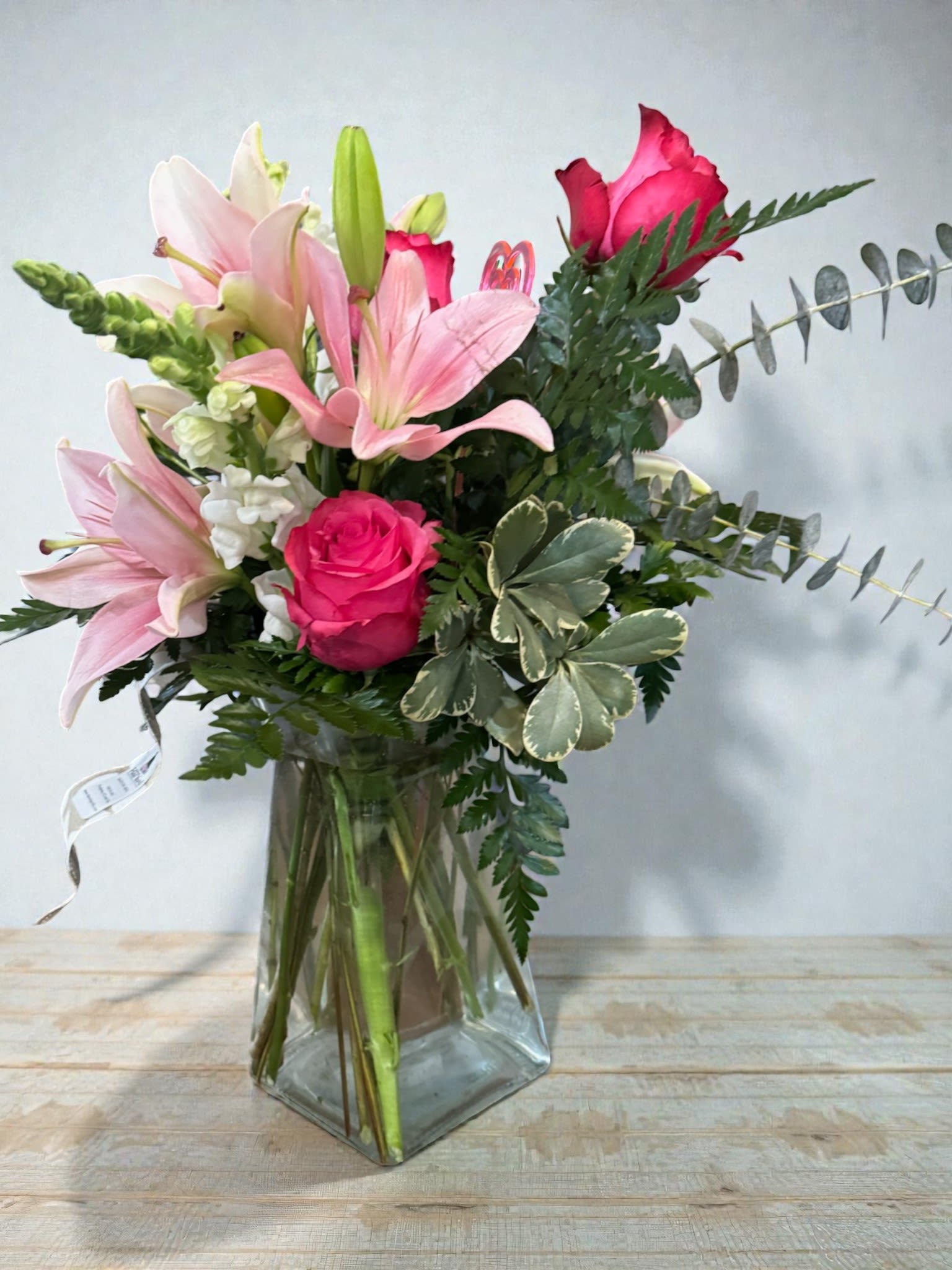 Pink lilies and roses arranged in a clear glass vase