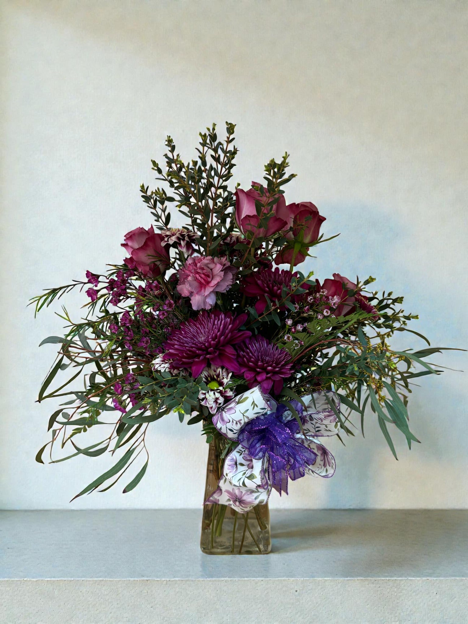 Purple and pink flower arrangement in a glass vase with a ribbon