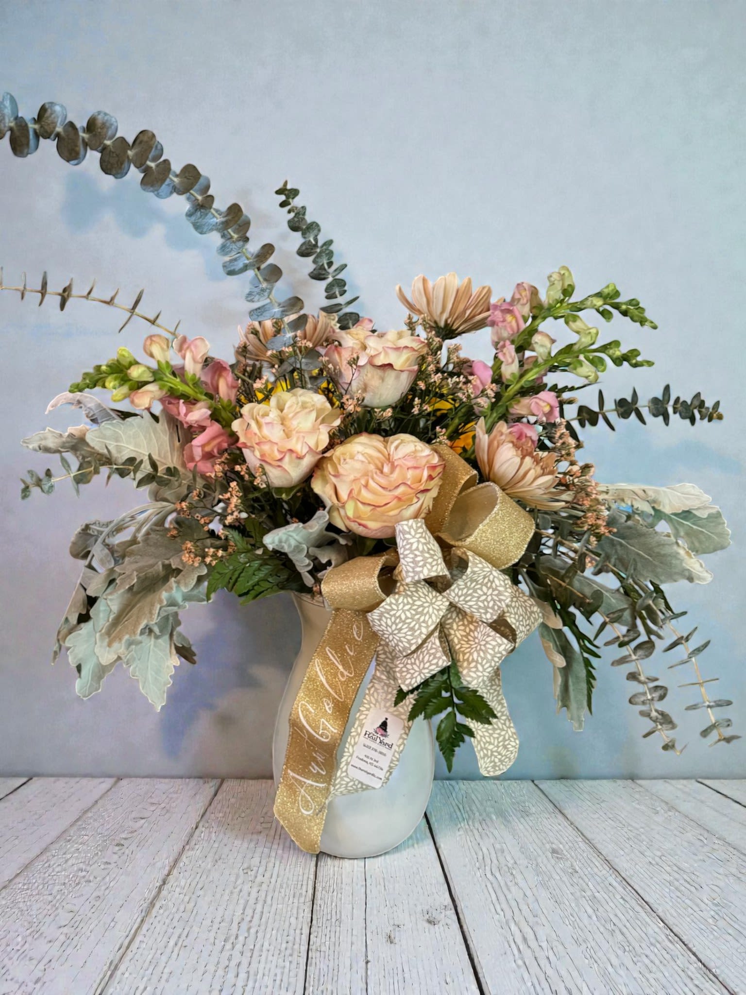 Blush roses and daisies in a white vase with a gold ribbon bow
