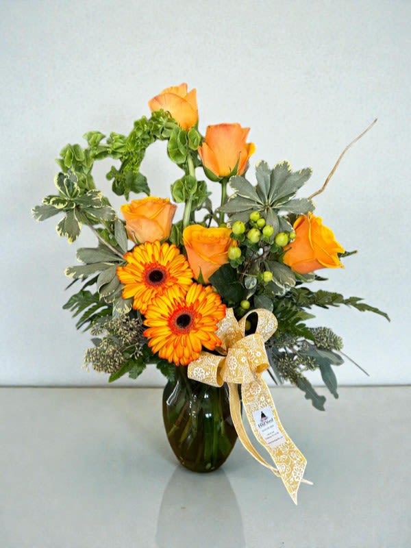 Orange roses and gerbera daisies in a glass vase with a ribbon