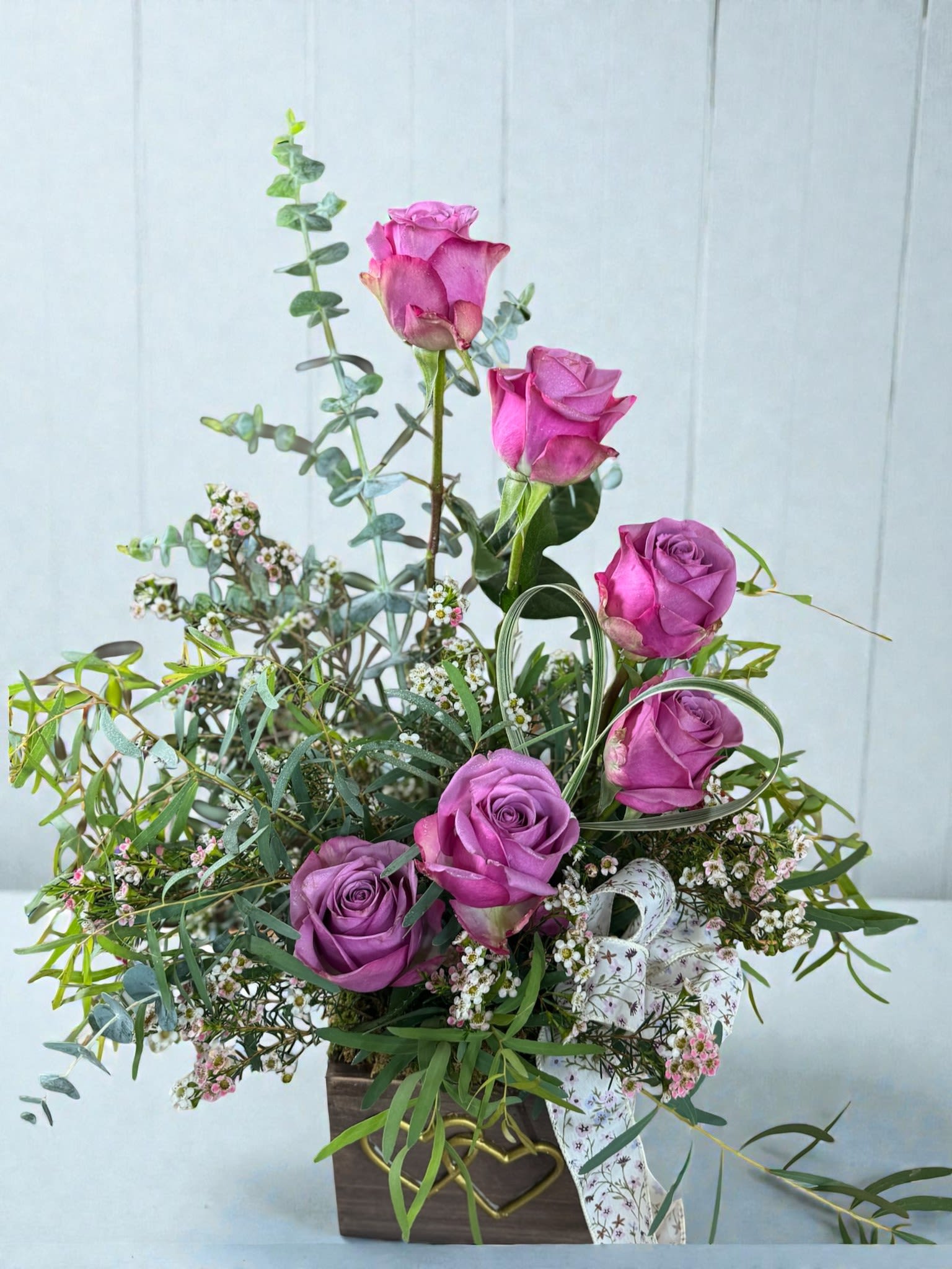 Purple roses in a wooden box with airy greenery and small white filler flowers