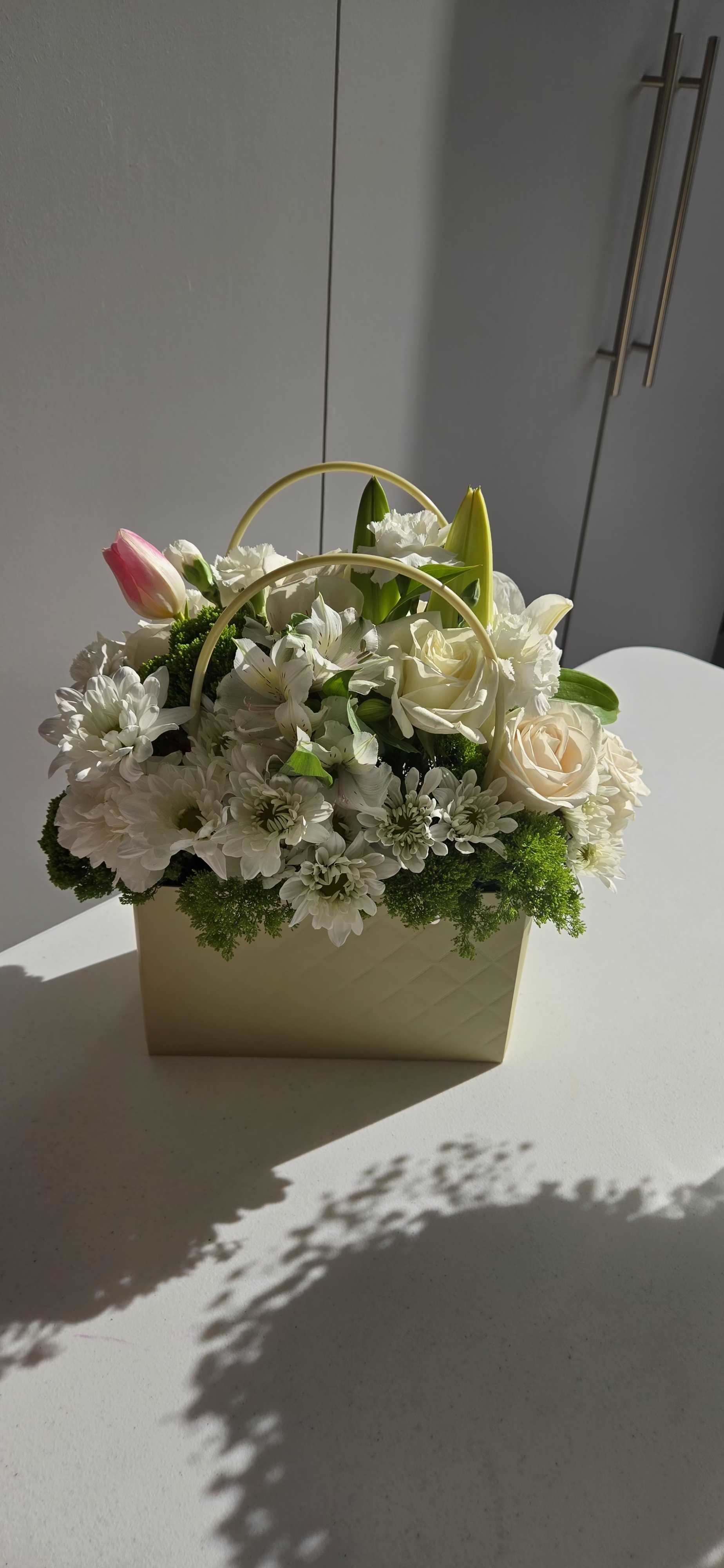 White floral arrangement in a cream handled box with pink tulip and roses