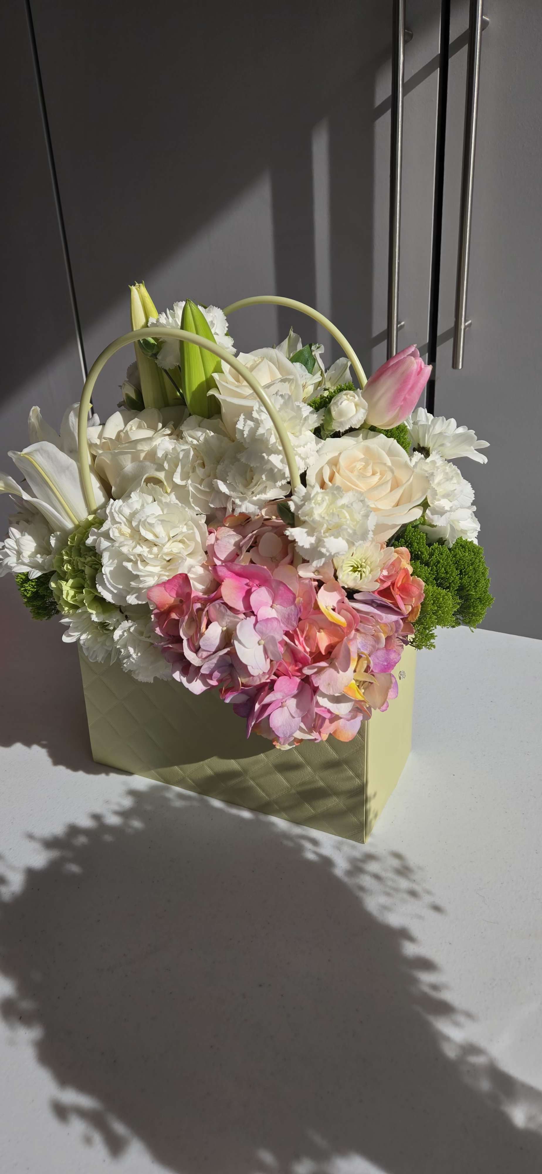 Mixed flower arrangement in a pale green gift bag with pink and white blooms
