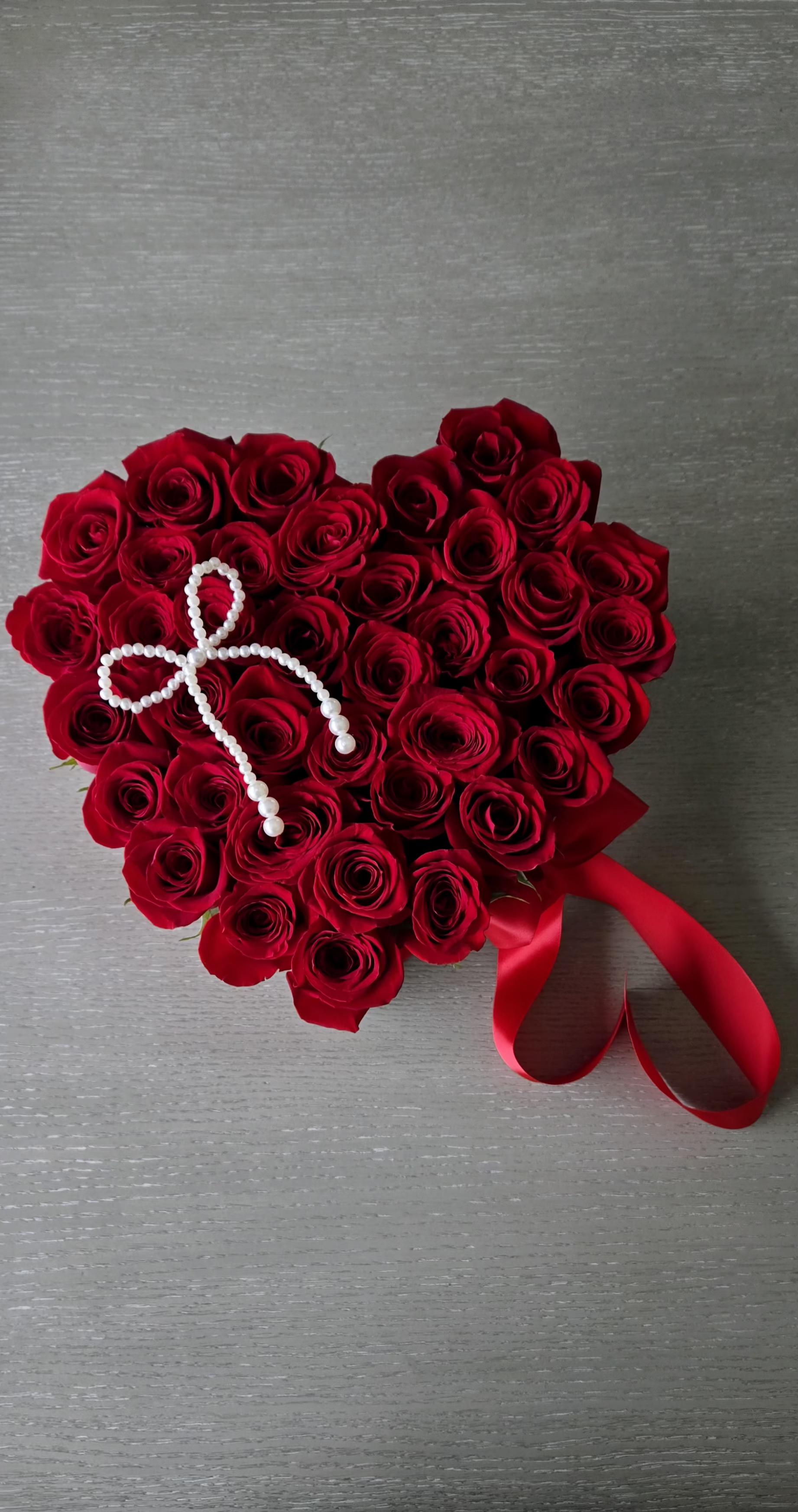 Heart-shaped bouquet of red roses with a pearl accent and red ribbon