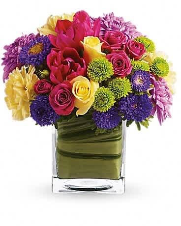 Colorful bouquet of roses, tulips, and mums in a square glass vase