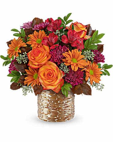Orange roses and mixed daisies in a woven basket vase