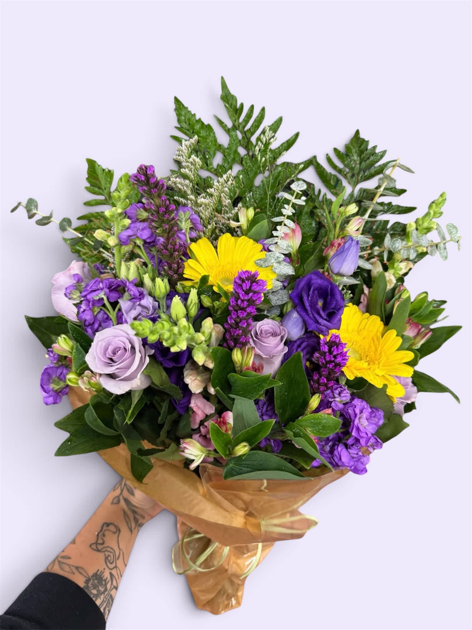 Hand-tied bouquet of purple and yellow flowers wrapped in brown paper