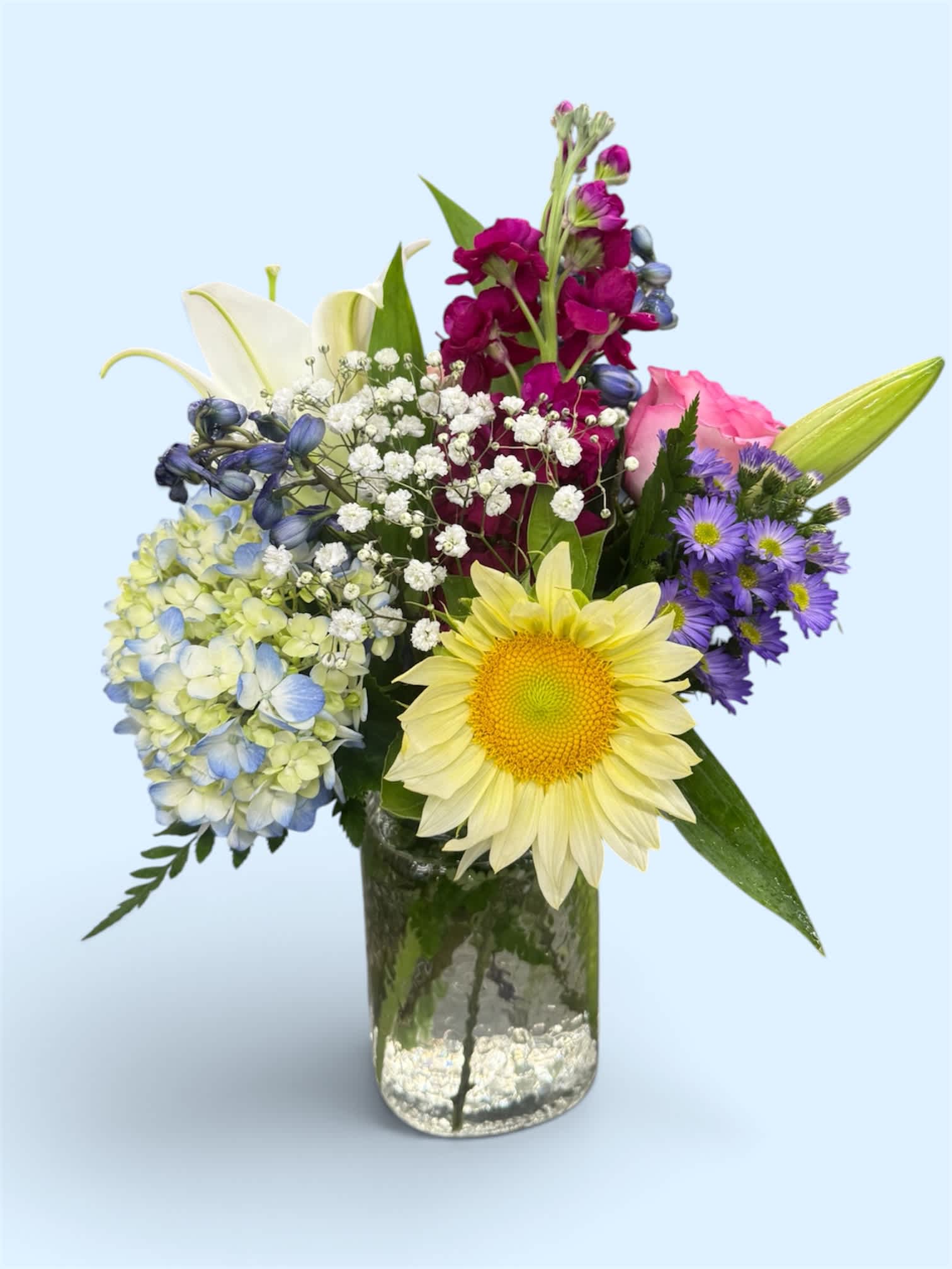 Mixed bouquet in a glass vase with a yellow sunflower, pink rose, and purple blooms