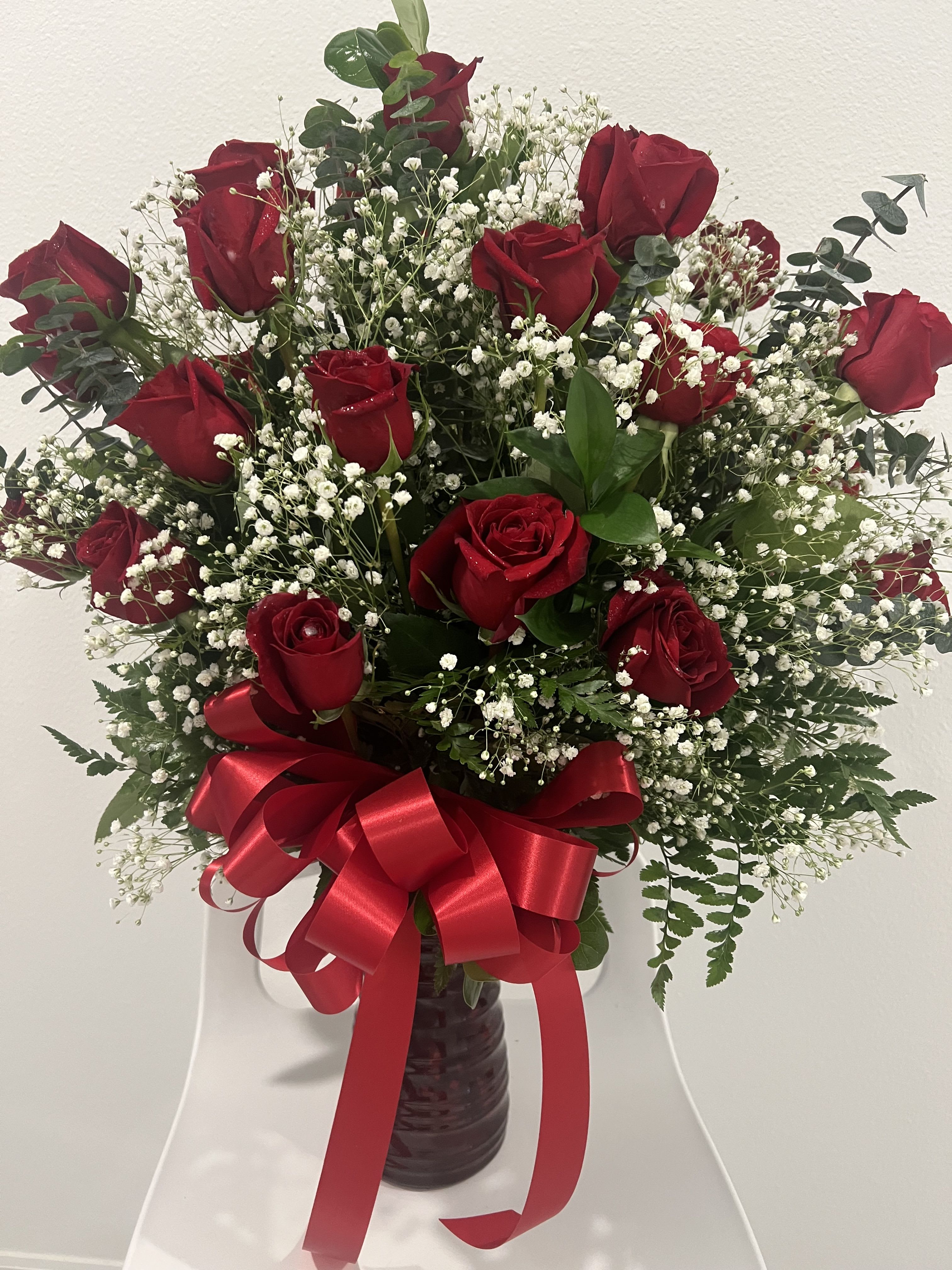 Red roses arranged in a vase with white baby's breath and a red ribbon bow.