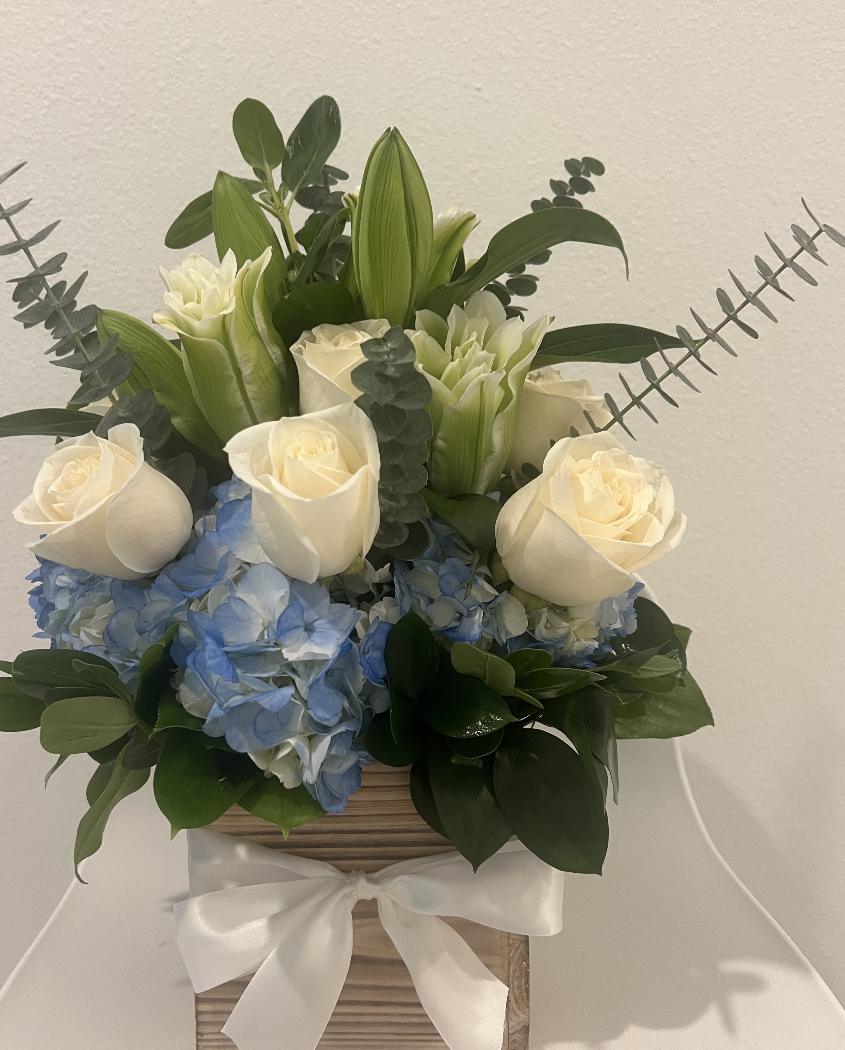 WHISPER OF LOVE - A graceful blend of blue, pure white roses, and elegant white lilies, this bouquet captures the essence of serenity and timeless beauty. Perfect for expressing love, celebrating special moments, or bringring peace and harmony to any occasion