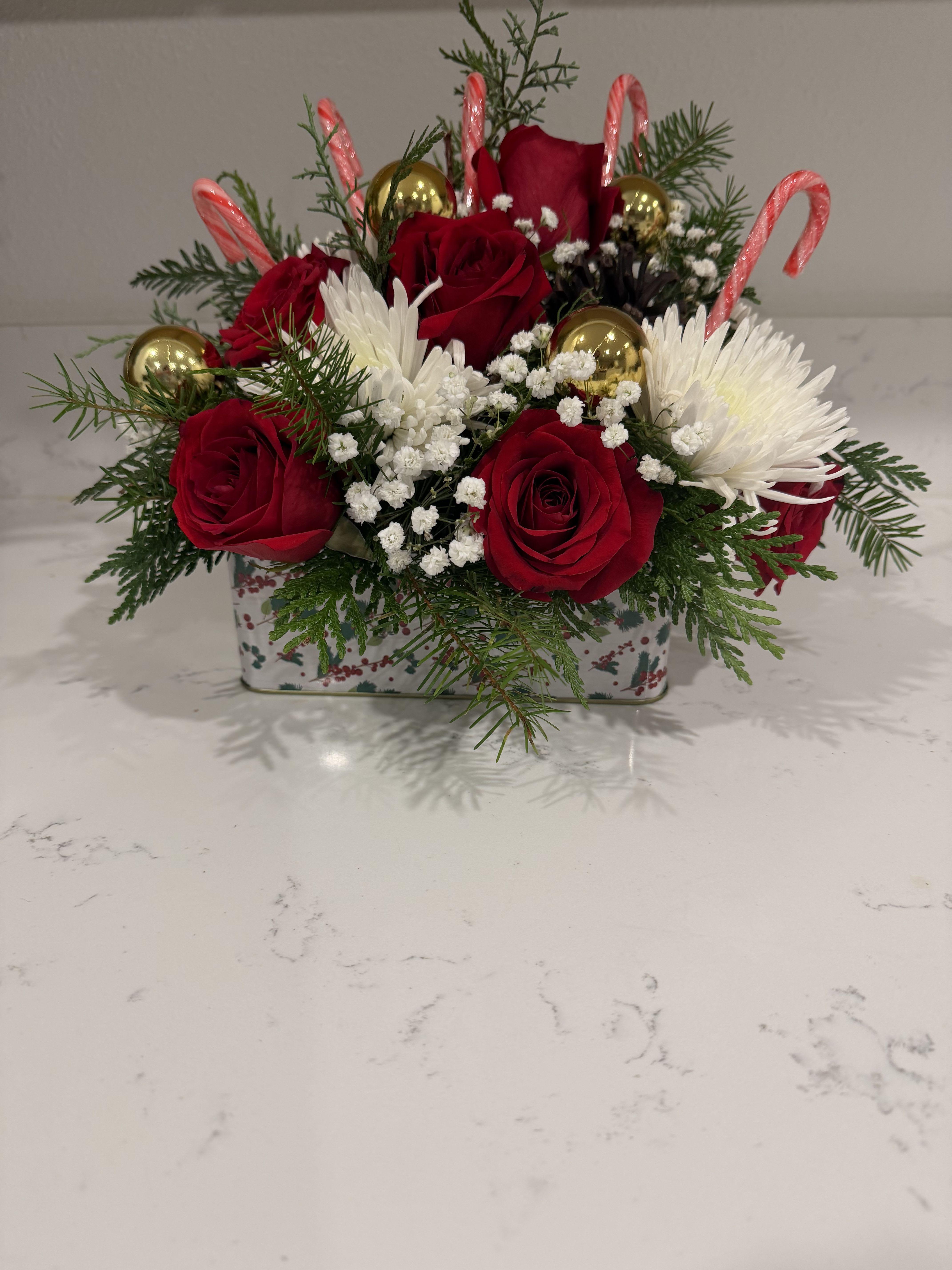 Golden Crimson Holiday Delight - Fresh red roses, delicate baby’s breath, and muscari blooms, accented with candy canes and gold ornaments, come together in this elegant rectangular Christmas container arrangement—perfect for gifting this Christmas.