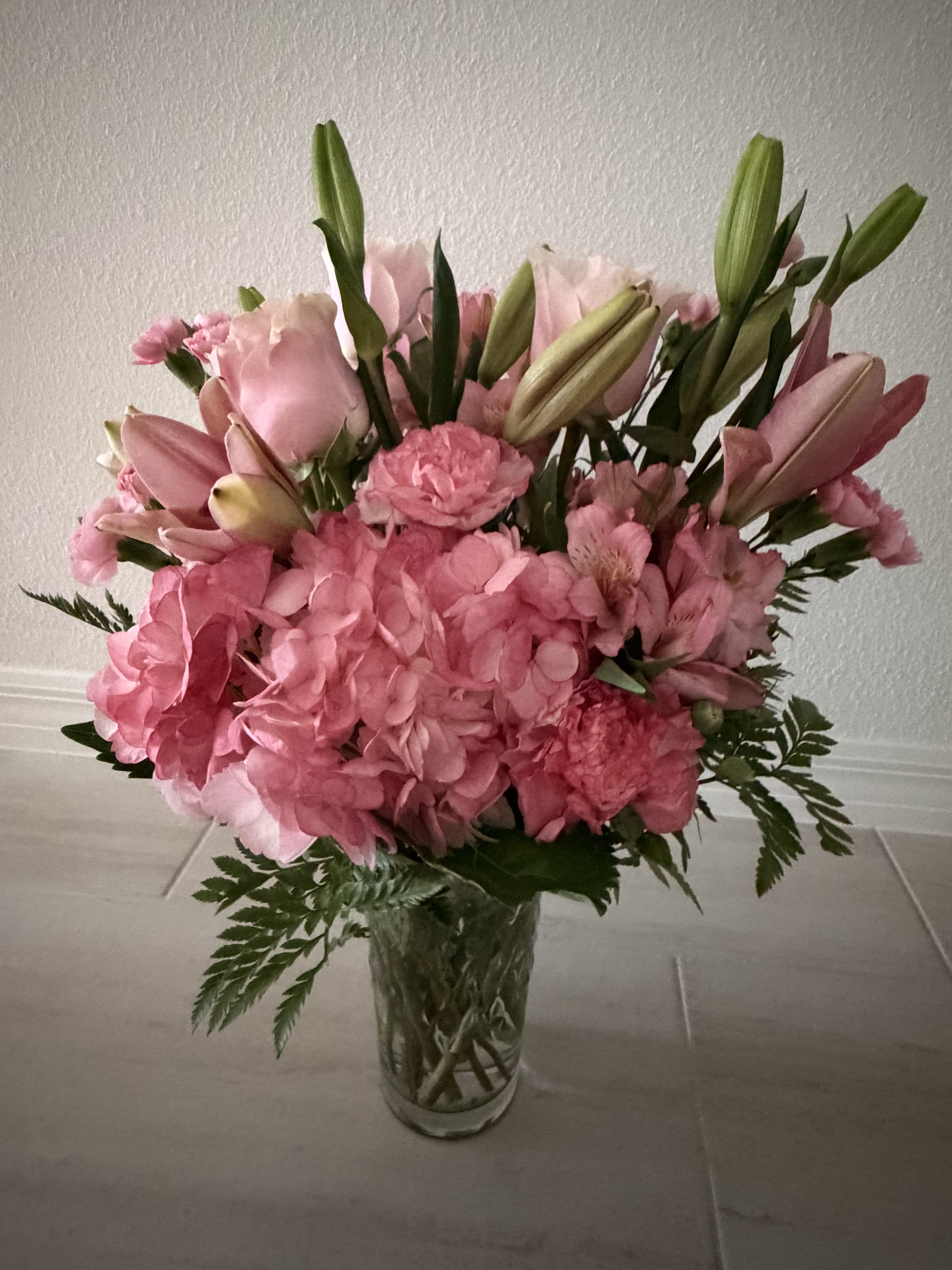 Pink bouquet with hydrangeas, lilies, and carnations in a clear glass vase