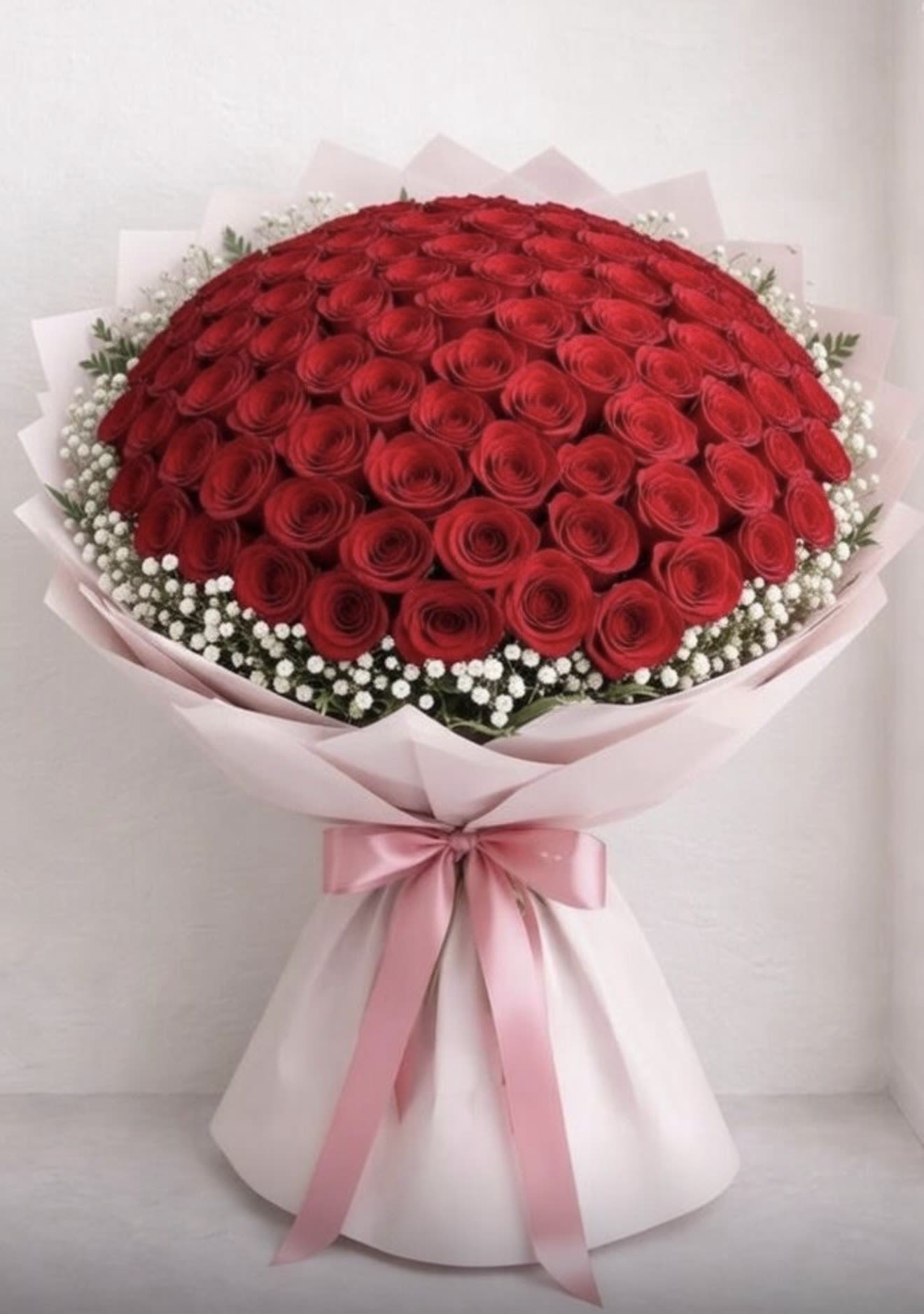 Large bouquet of red roses wrapped in pink paper with a pink ribbon