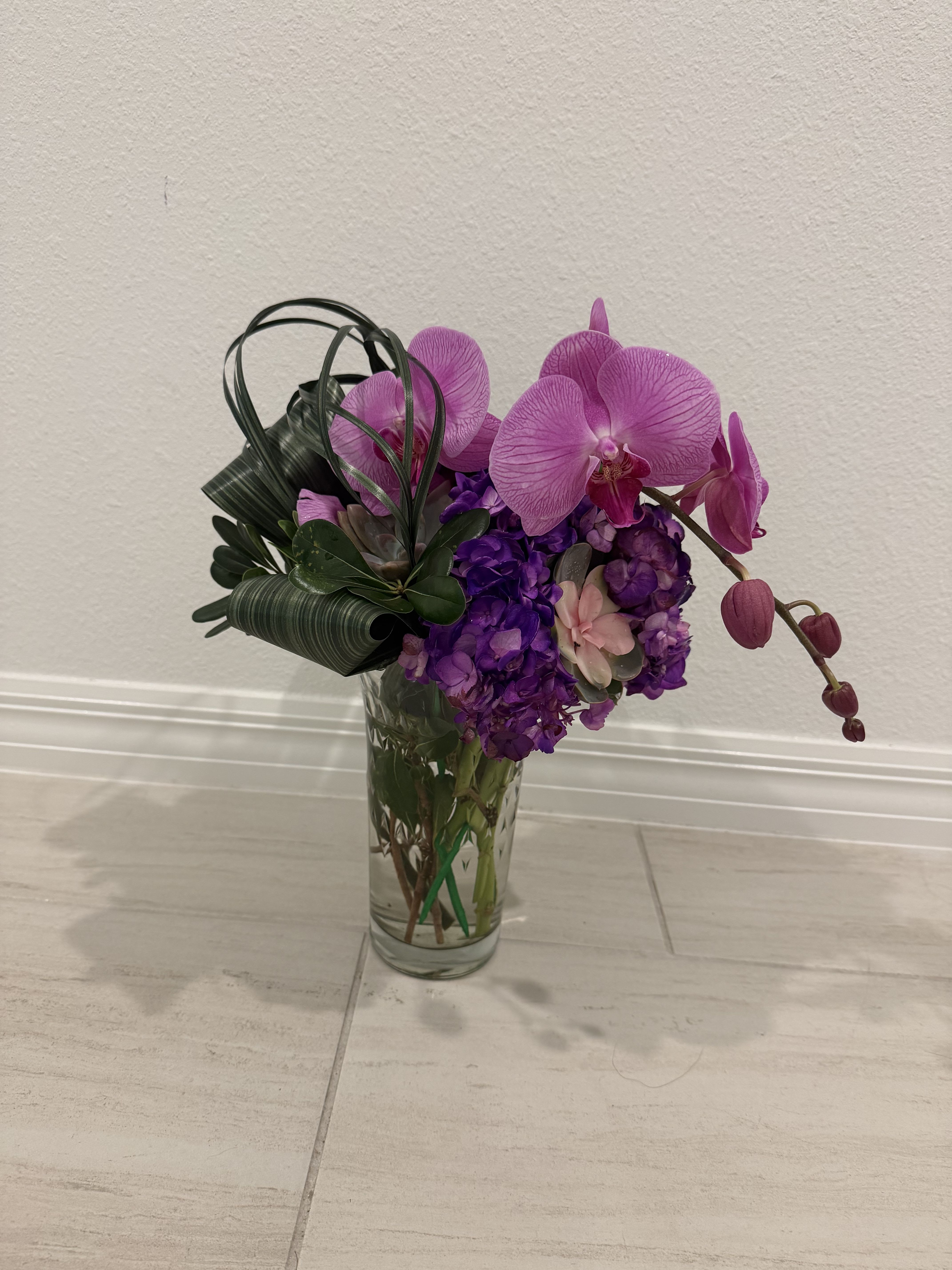 Purple orchids and hydrangeas arranged in a clear glass vase