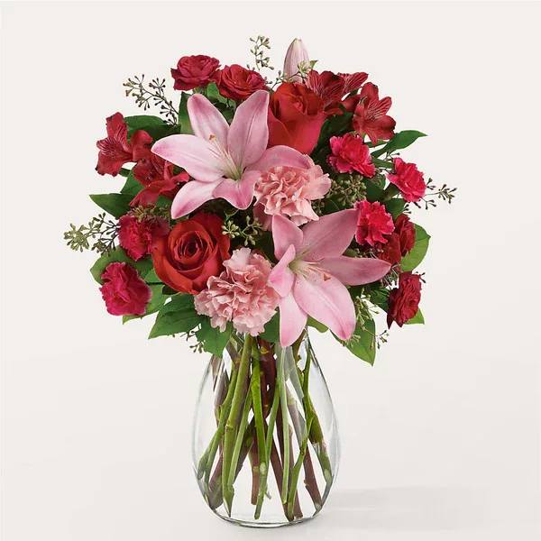 Bouquet of pink lilies, red roses, and carnations in a clear glass vase