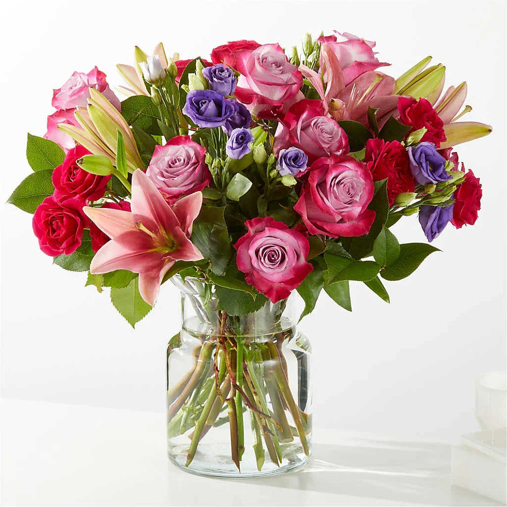 Bouquet of pink and purple roses with lilies in a clear glass vase