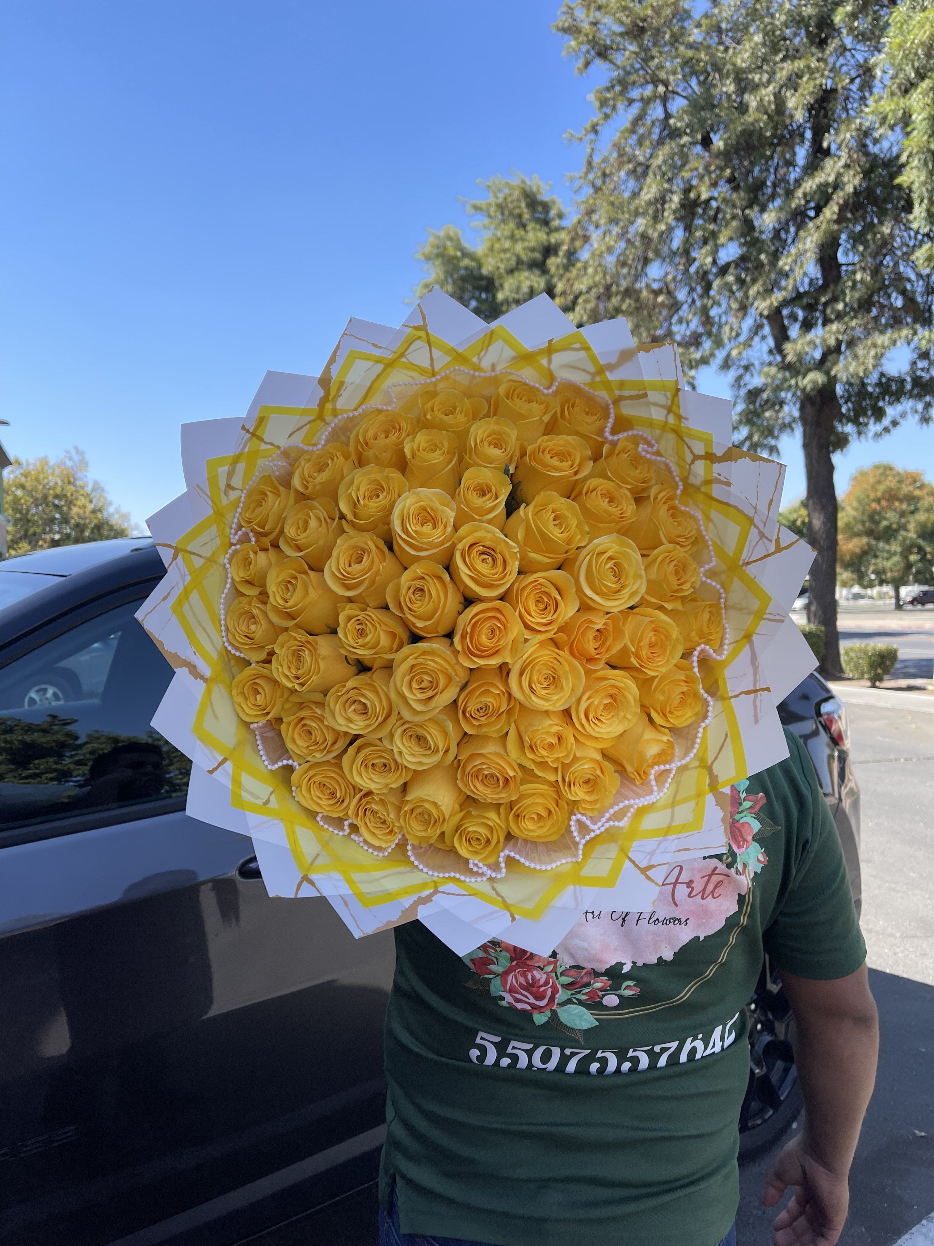 Sunshine Buchón  - A dense dome of fifty long-stem yellow roses creates an immediate burst of sunny warmth-perfect as a Día de las Flores Amarillas bouquet or a joyful celebration arrangement. The tightly clustered roses form a full, rounded buchón that greets the recipient with bold color and an unmistakable message of friendship and bright affection; she'll feel genuinely celebrated the moment the wrapping unfolds.  Wrapped in layered white and yellow paper, the graphic contrast frames the blooms and keeps the focus on those vibrant yellow roses while hints of white in the wrap echo the bouquet's clean, uplifting mood. A delicate pearl garland trims the edge for a touch of texture and quiet elegance, making this large flower arrangement appropriate for festive occasions, thank-yous, or to lift someone's spirits. Approximately fifty long stems, arranged in a compact dome-care instructions: keep in fresh water, trim stems every few days, and avoid direct midday sun to preserve bloom life. Available for delivery in Madera, CA.