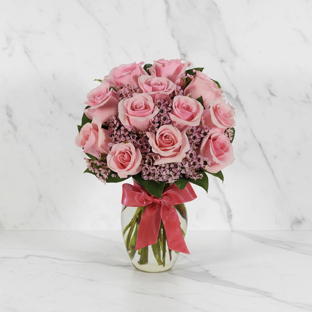 Pink rose bouquet in a clear glass vase with a red ribbon