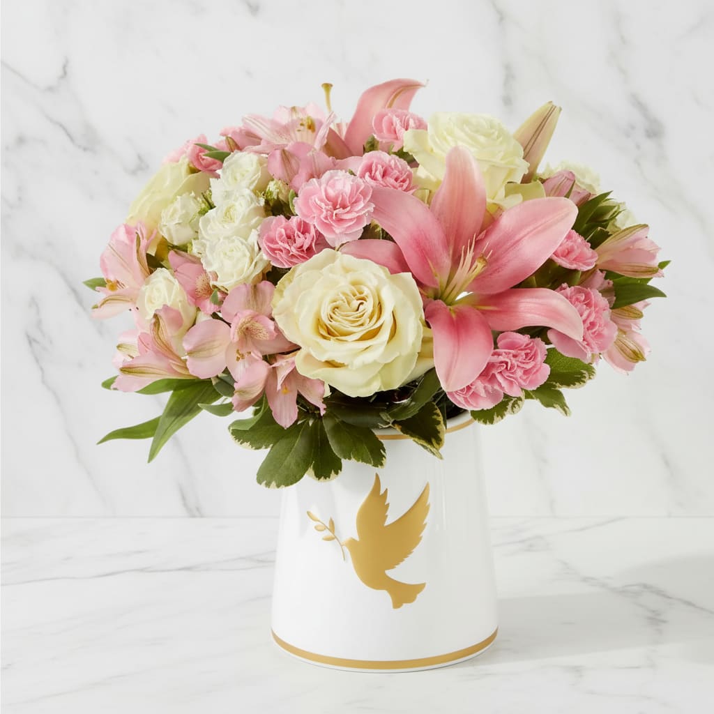 Pink and white flowers arranged in a white vase with a gold dove design.