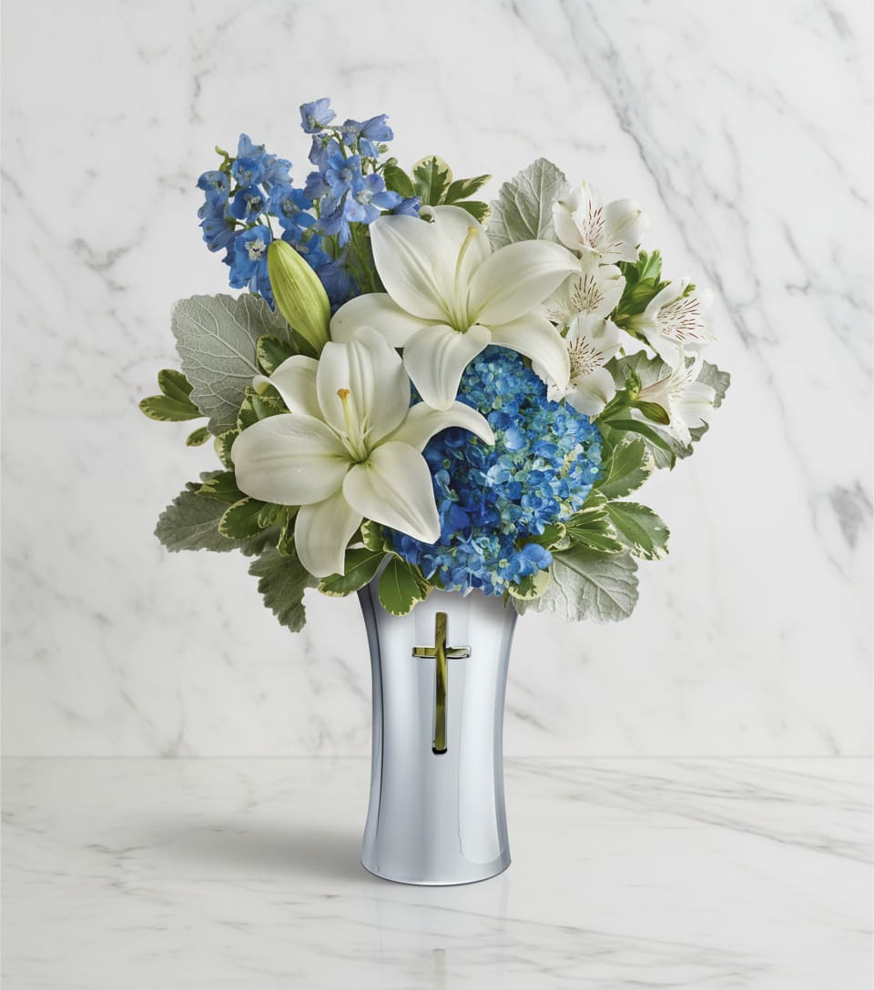 White lilies and blue flowers in a silver vase with a cross