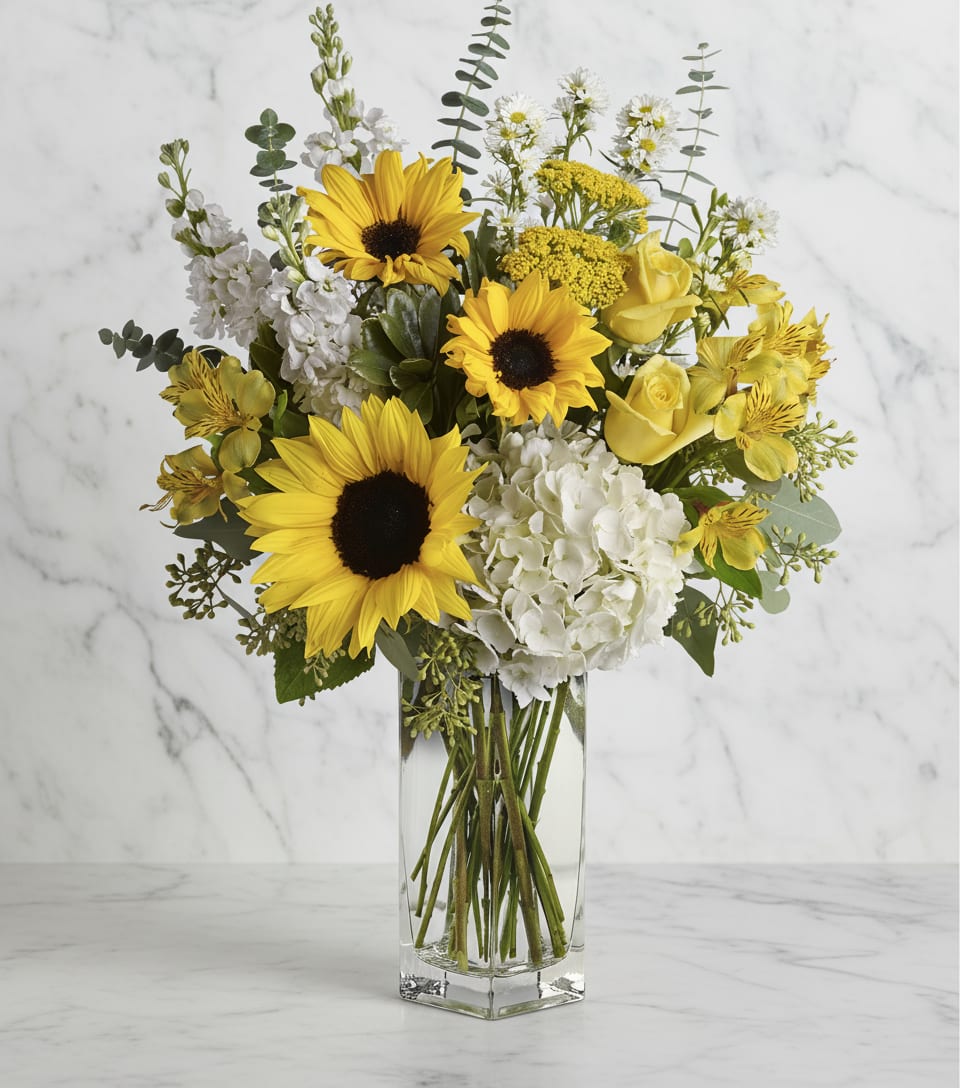 Yellow sunflowers and white flowers arranged in a clear glass vase