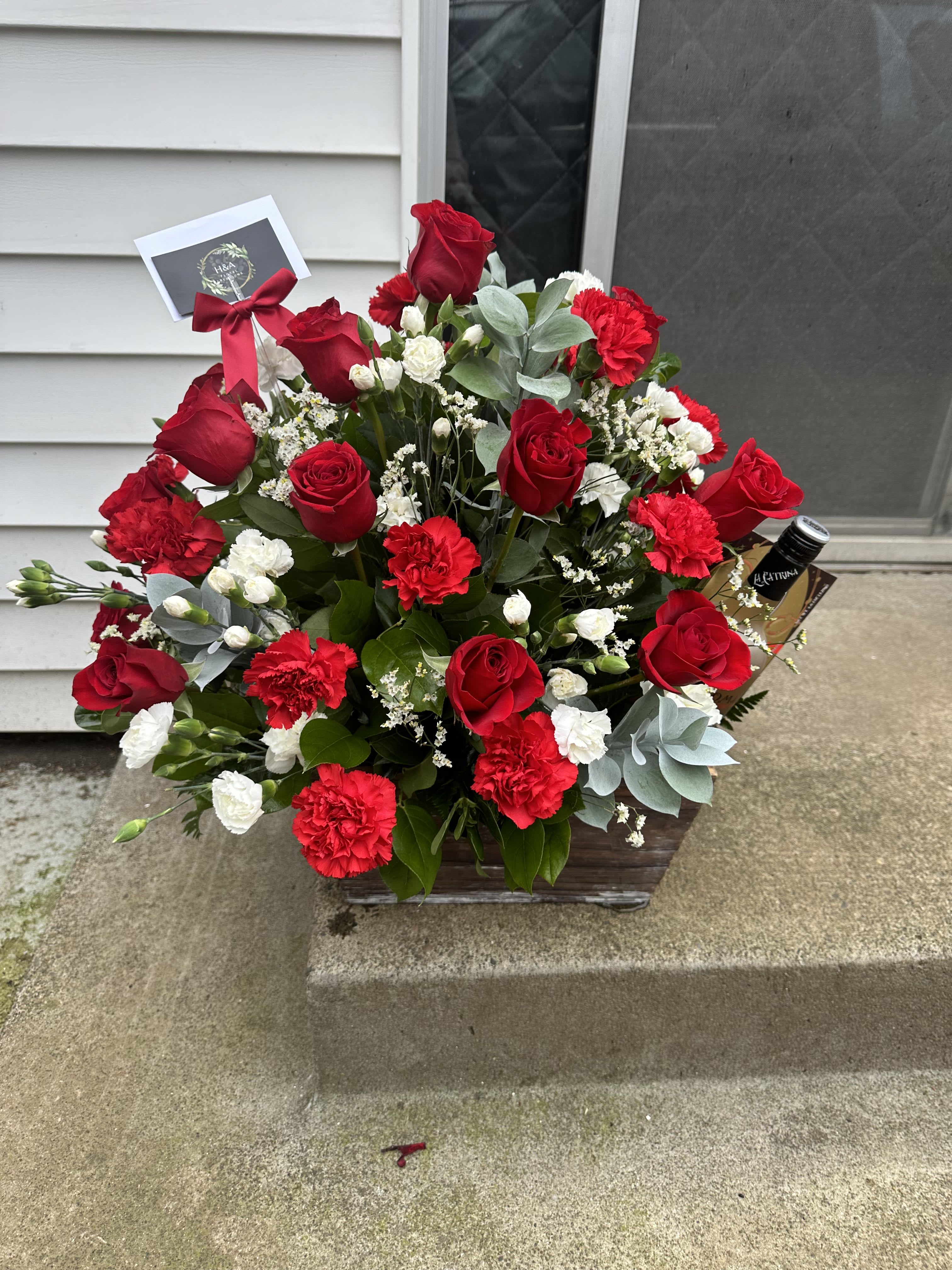 Red roses and carnations in a wooden basket with a ribbon and card.