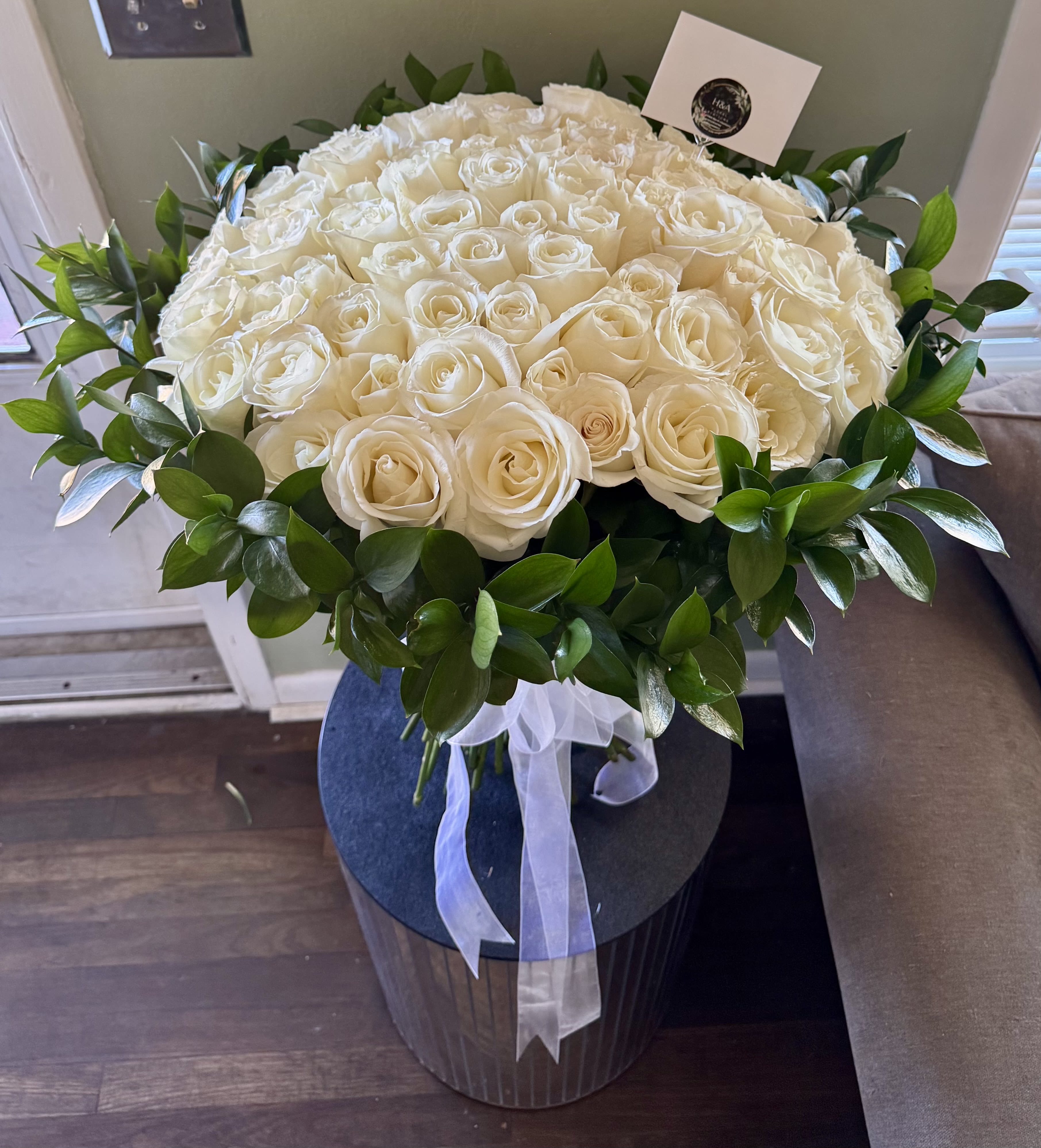 Large bouquet of white roses with a green leaf border and white ribbon