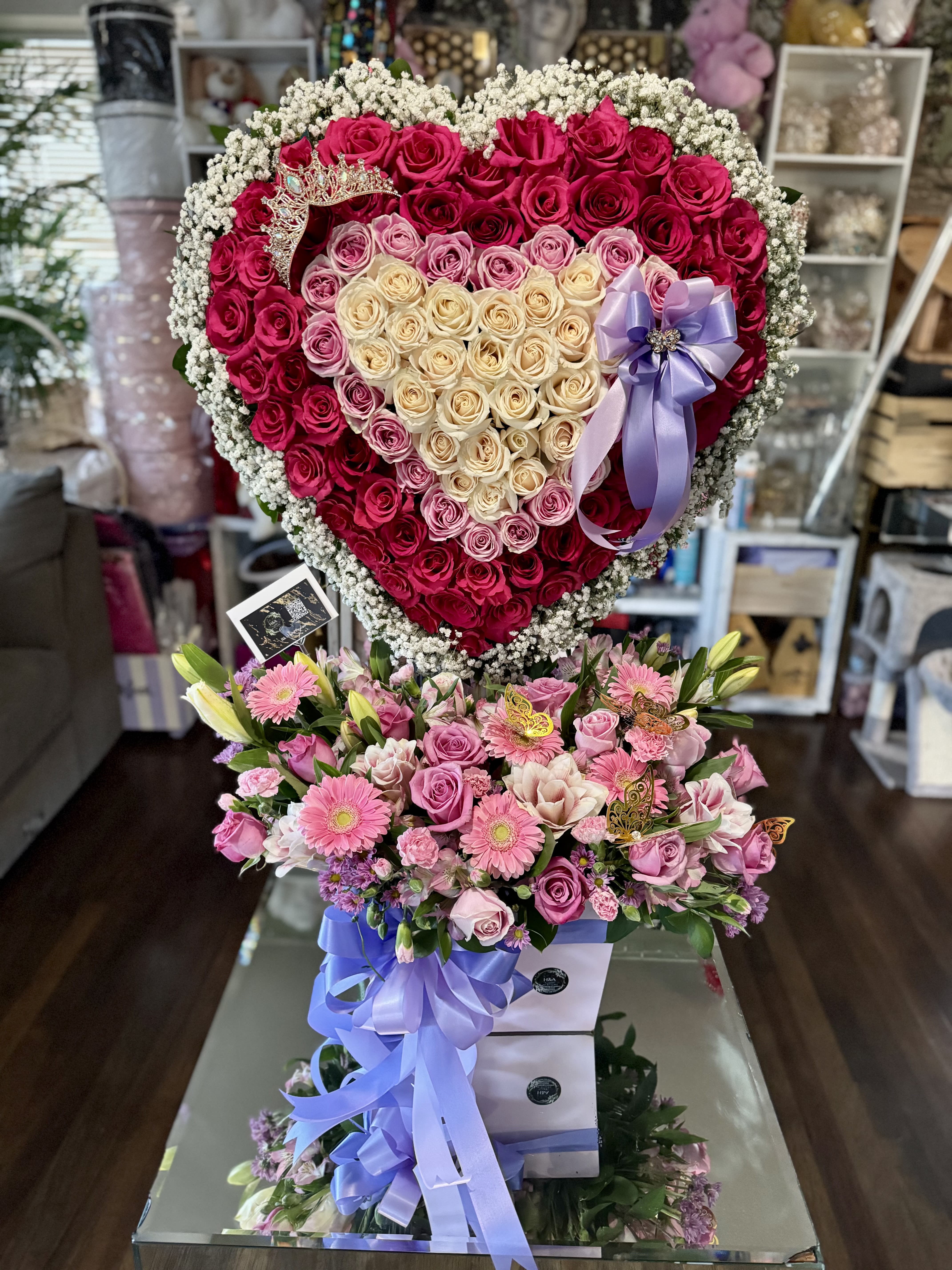 Heart-shaped rose arrangement with a purple ribbon and crown topper