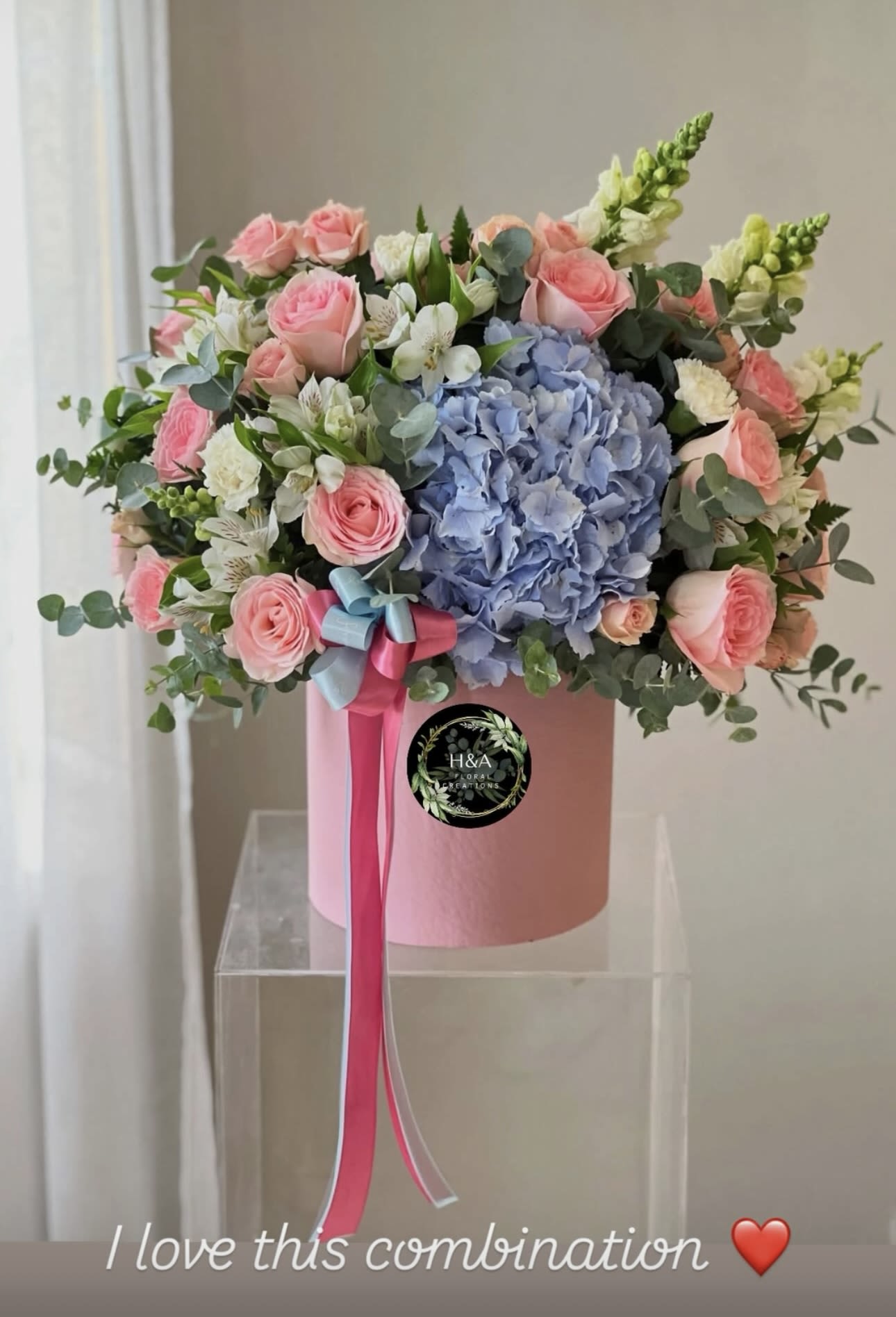 Pink roses and blue hydrangea in a pink hatbox with ribbon
