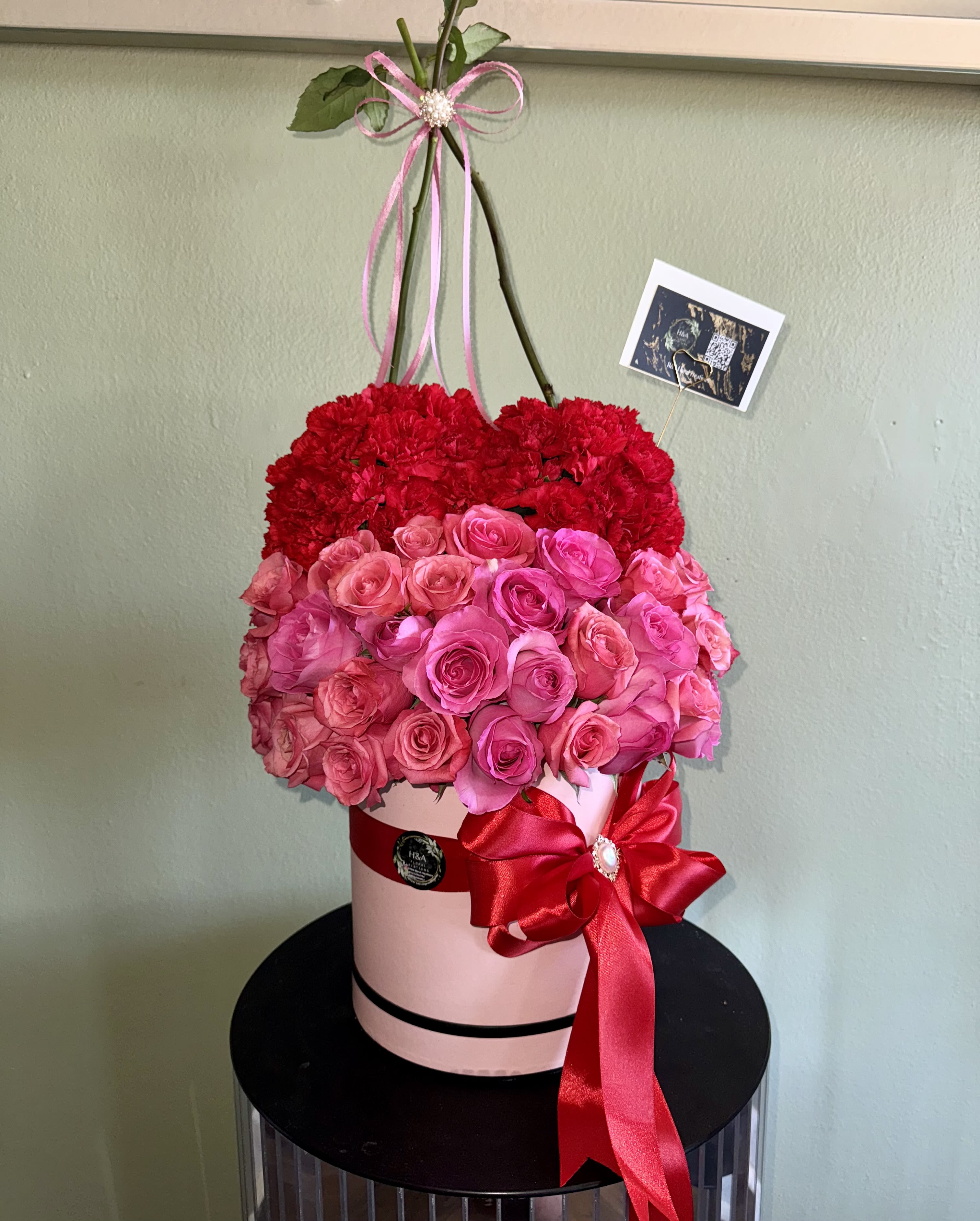 Heart-shaped floral arrangement of red carnations and pink roses in a pink box