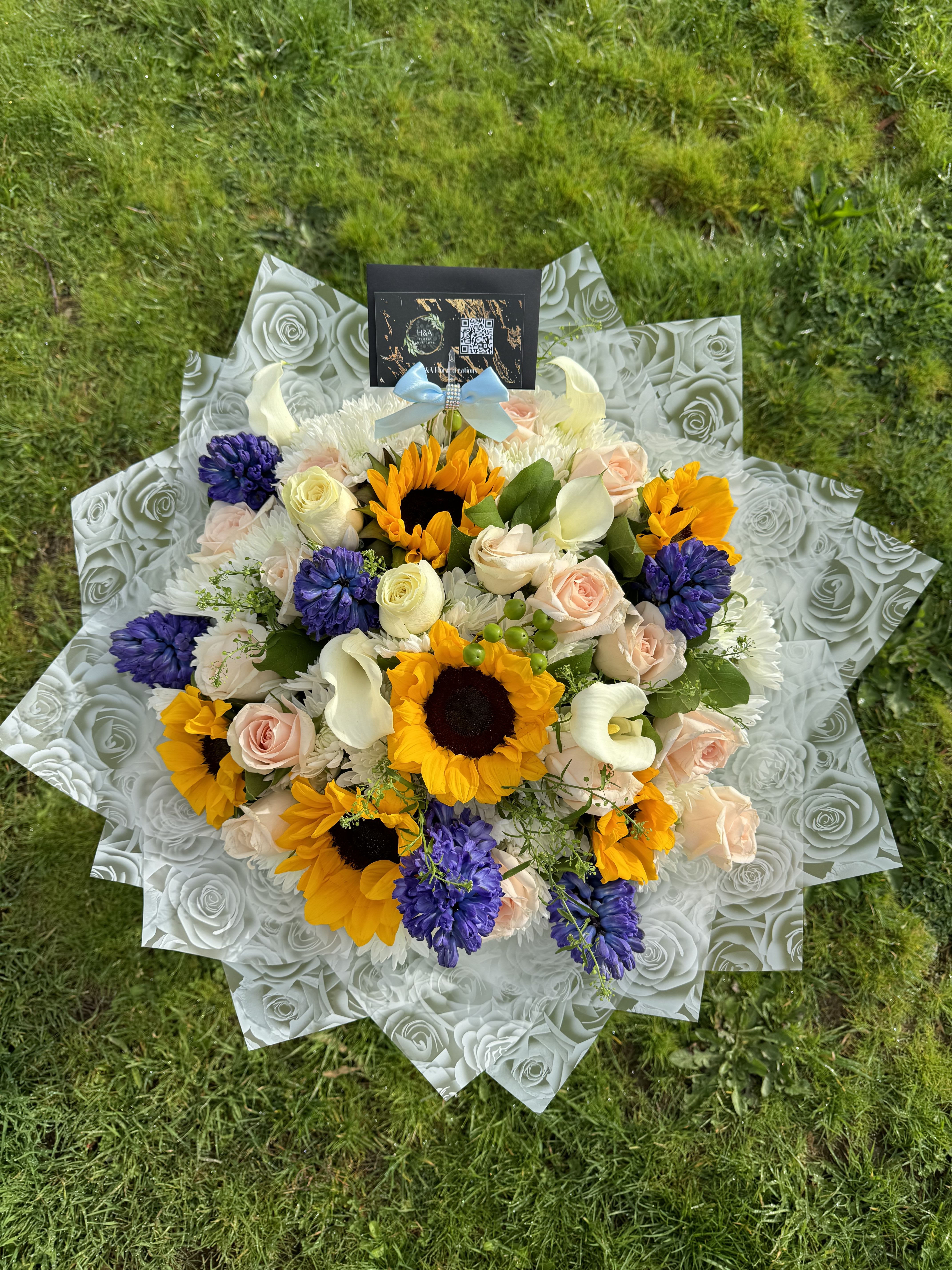 Bouquet of sunflowers, roses, and purple blooms wrapped in patterned paper