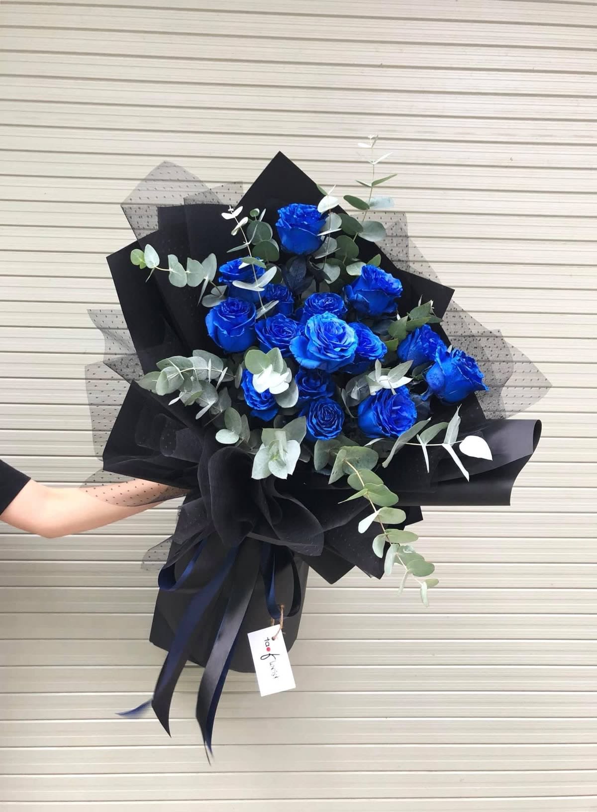 Bouquet of vivid blue roses with eucalyptus in black wrapping