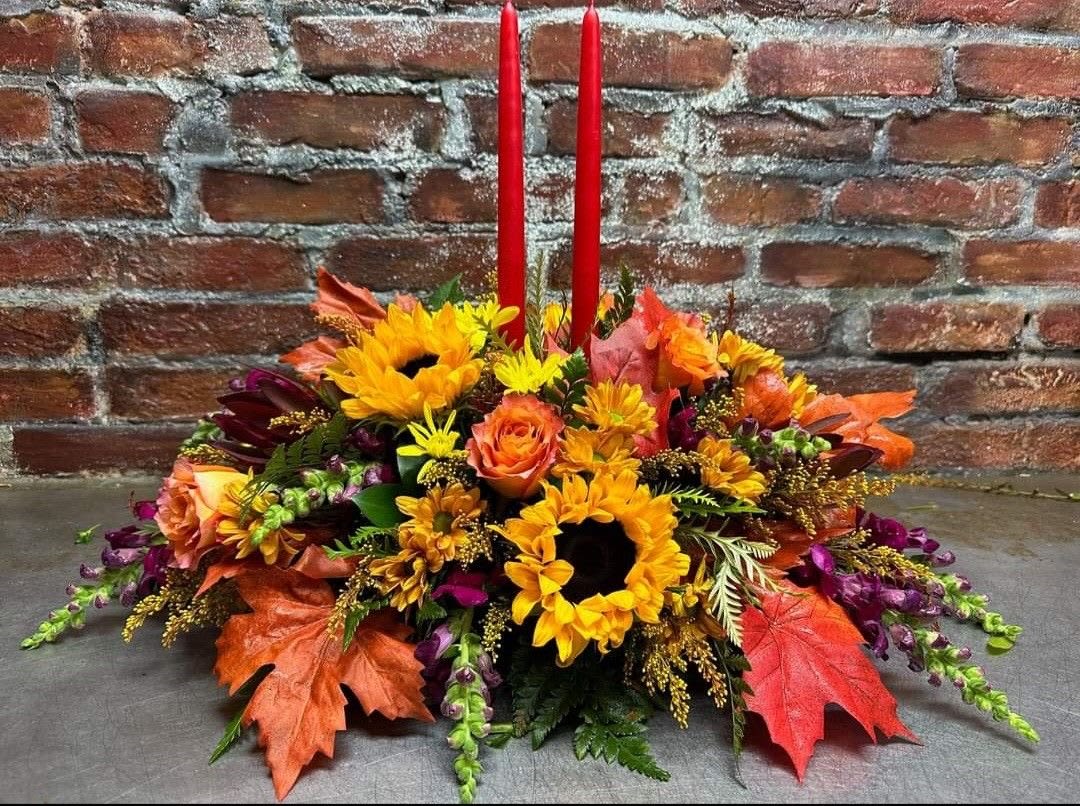 Autumn floral centerpiece with sunflowers, roses, and red taper candles