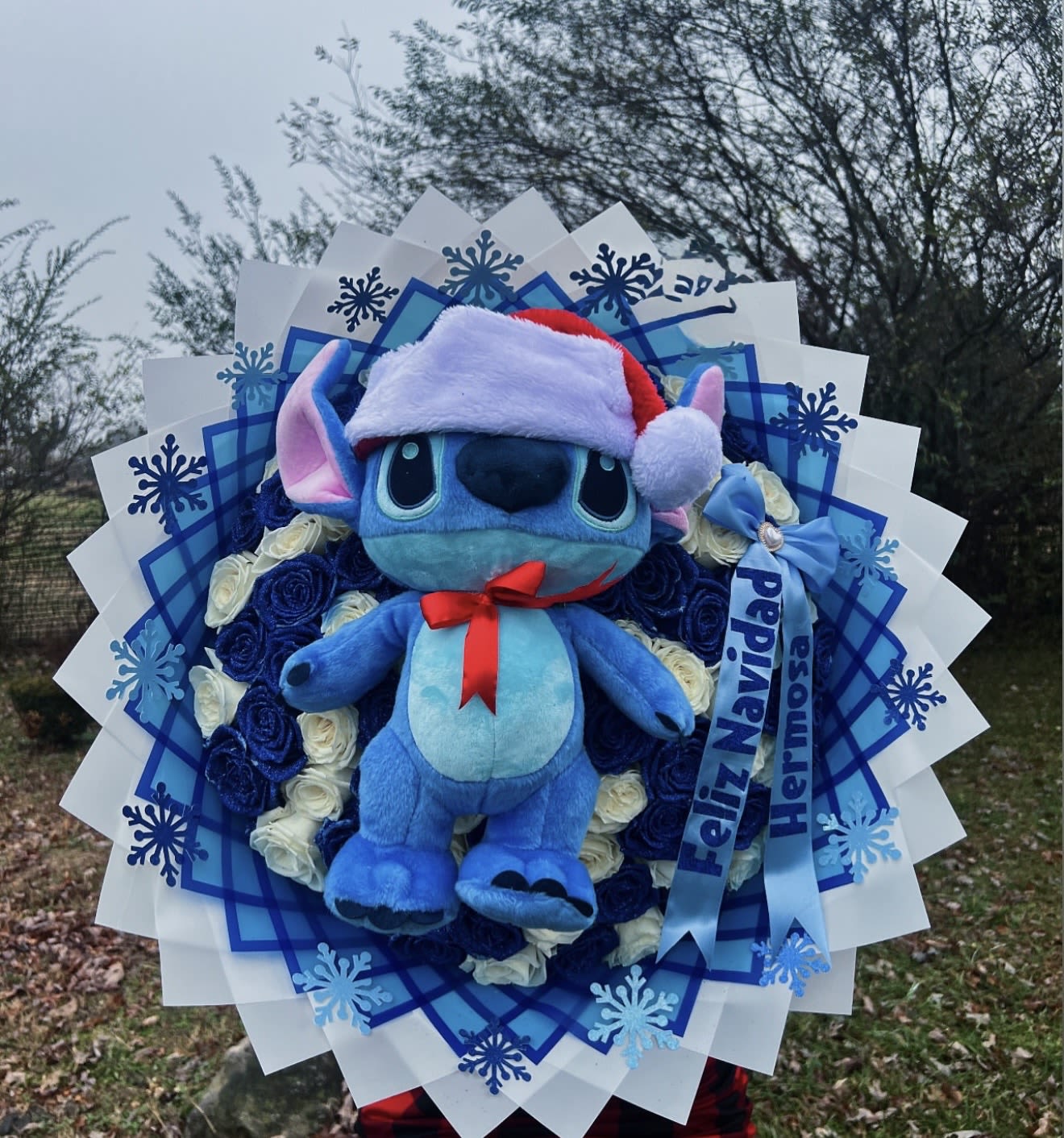 Blue plush character in a Santa hat surrounded by blue and white roses