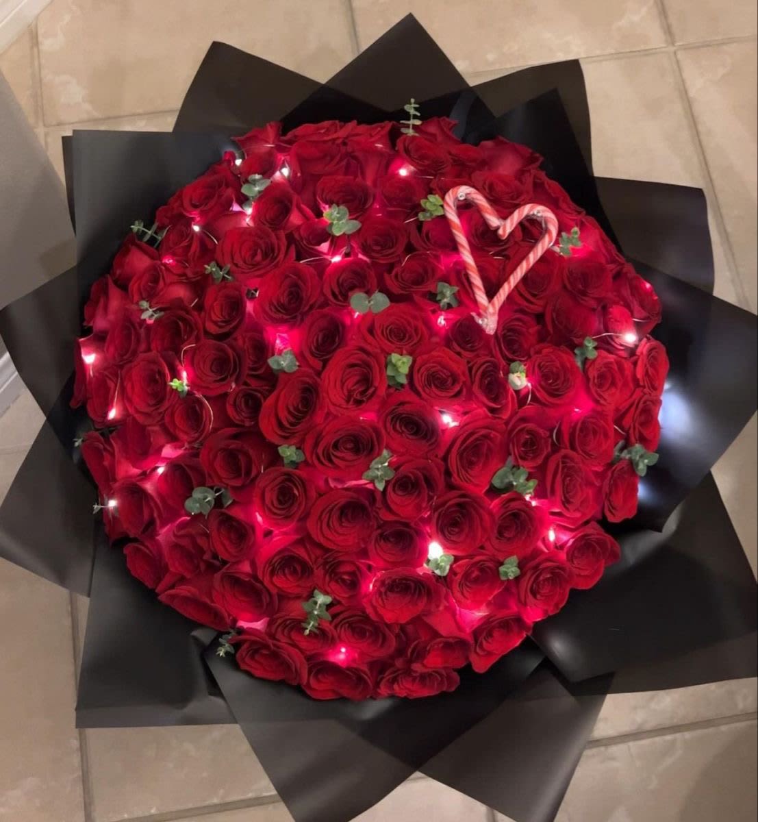 Large bouquet of red roses wrapped in black paper with a candy cane heart