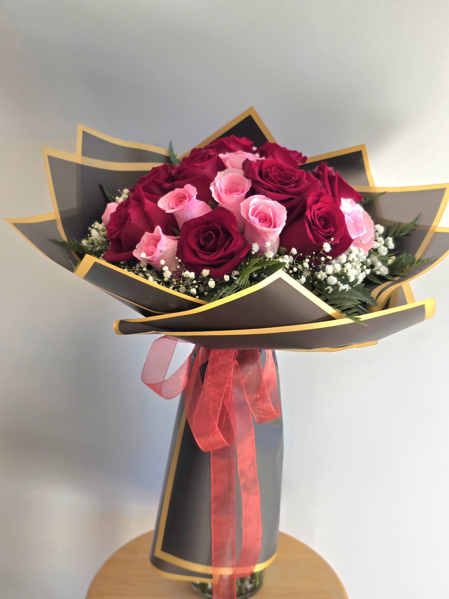 Bouquet of red and pink roses wrapped in black paper with a pink ribbon