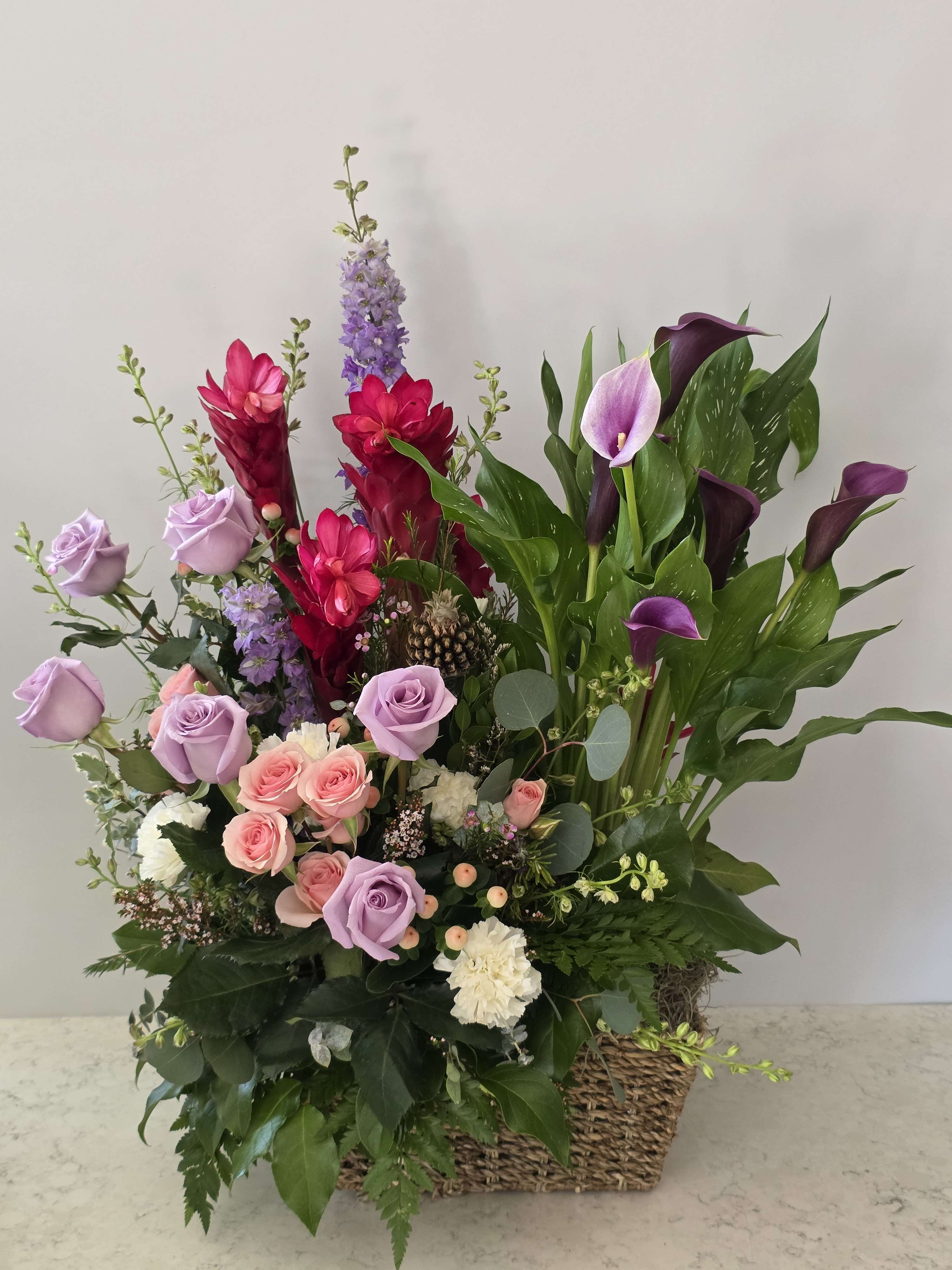 Mixed bouquet with roses, calla lilies, and purple flowers in a woven basket