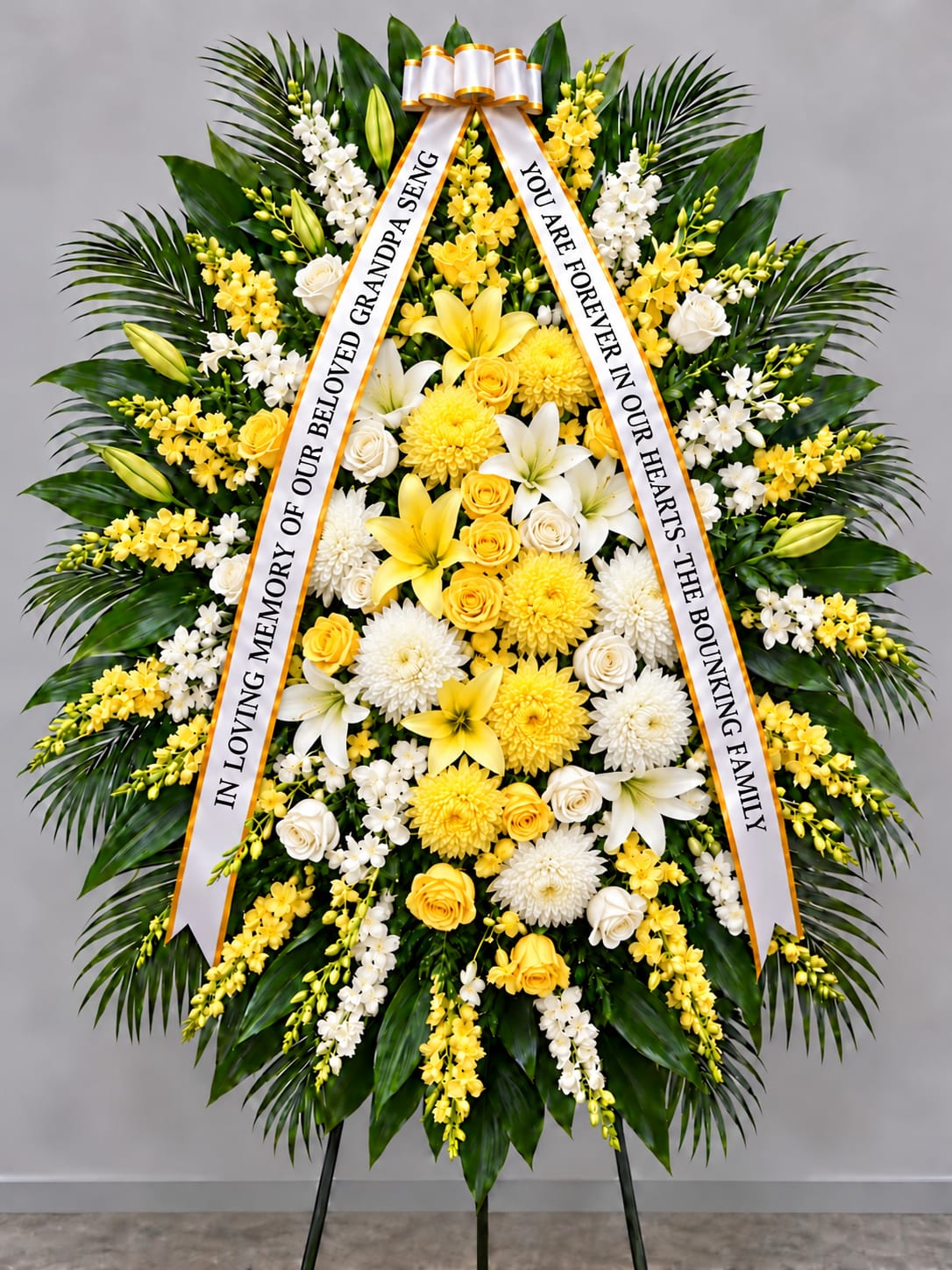 Standing funeral wreath of yellow and white flowers with memorial ribbons