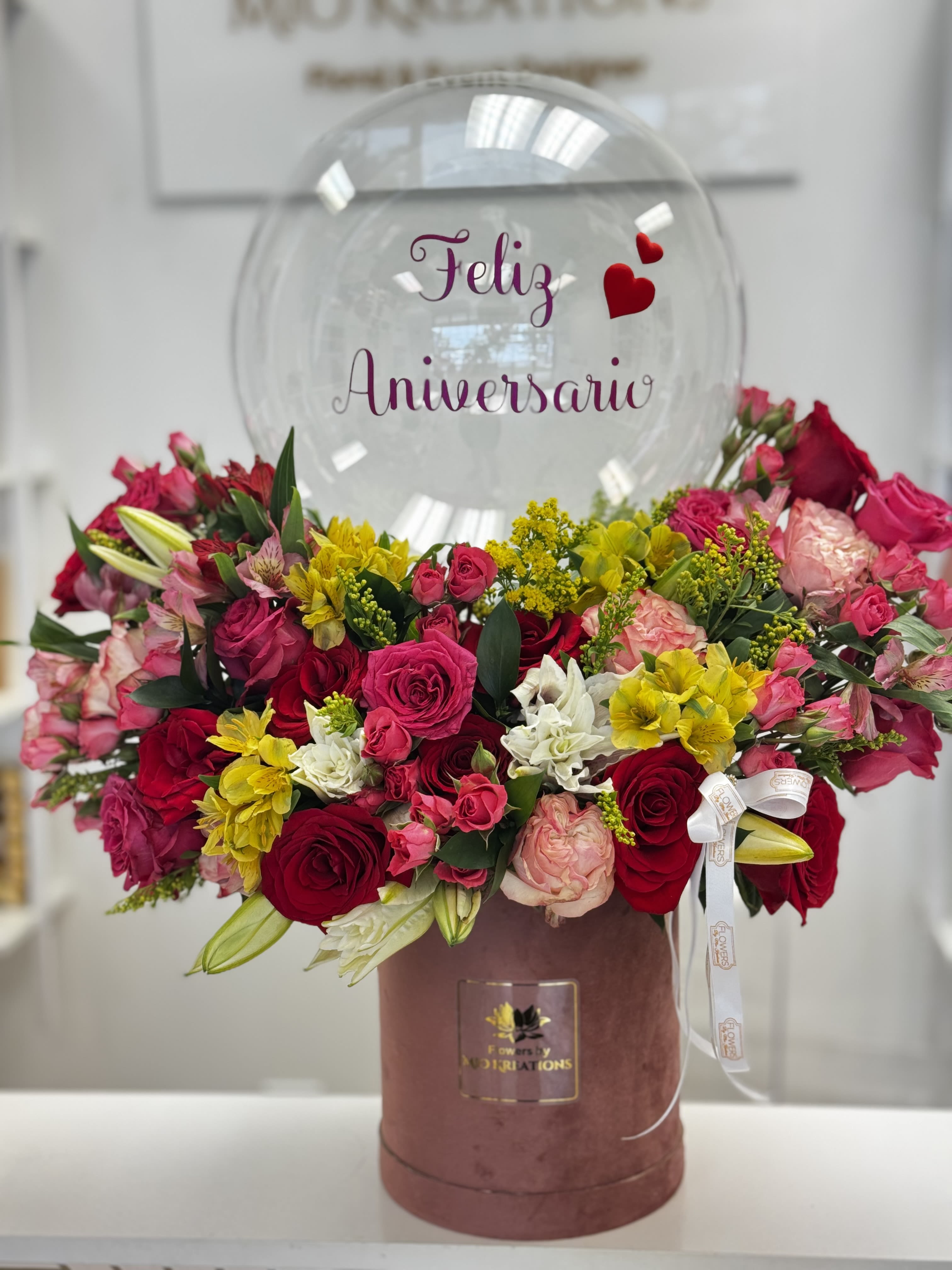 Mixed pink, red, yellow, and white flowers in a pink box with a clear anniversary balloon.